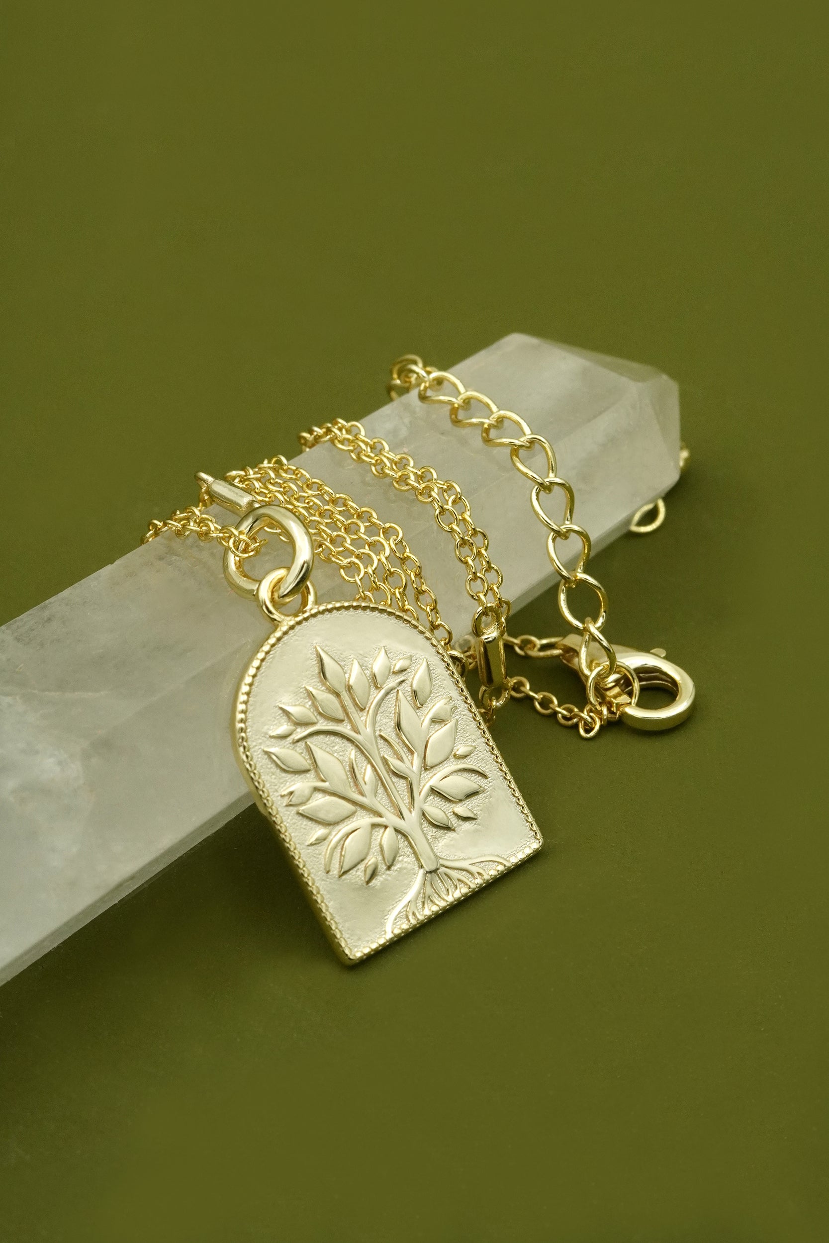 Gold necklace with a tree pendant on a green background