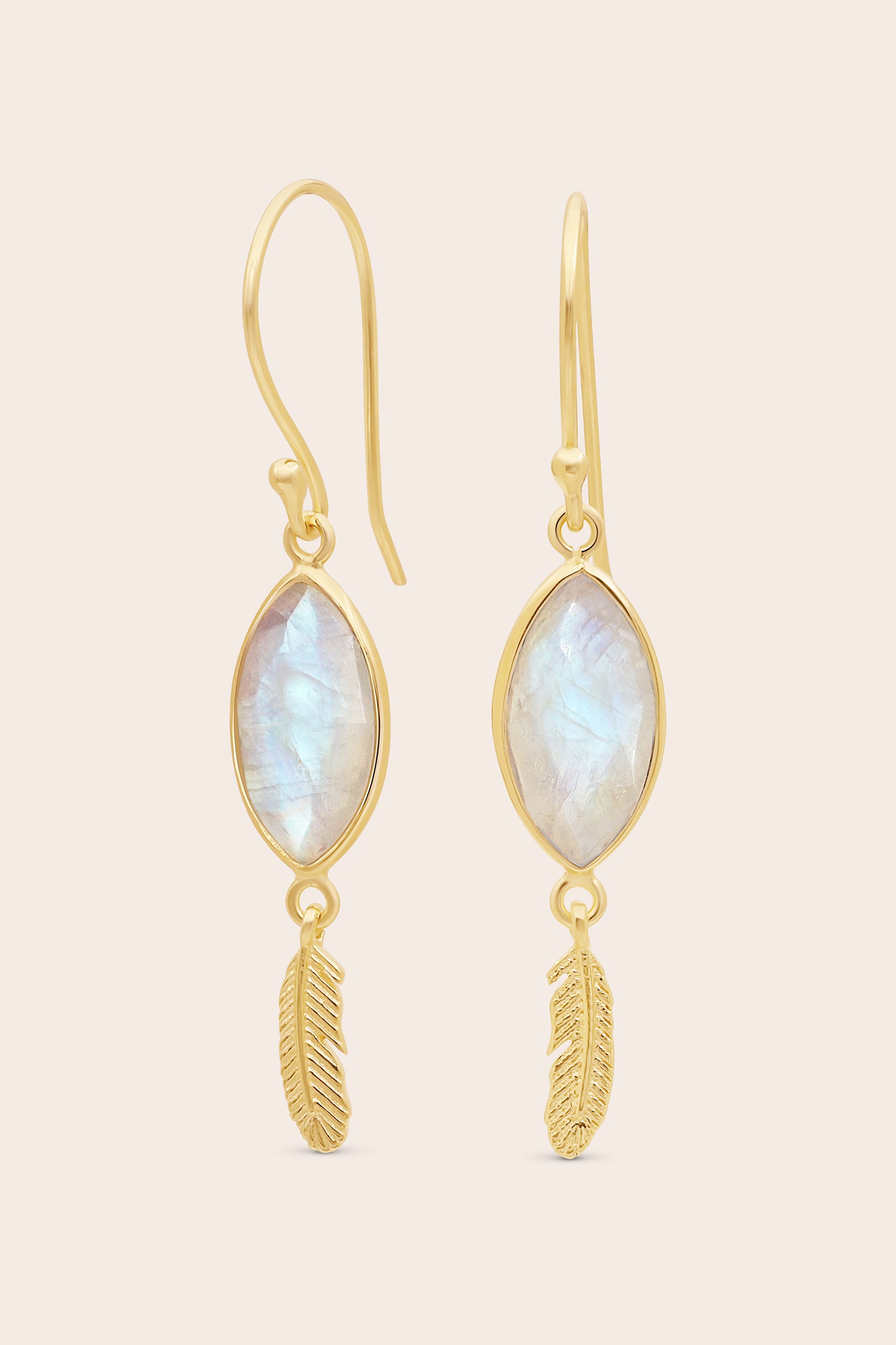 Gold earrings with moonstone stones and feather designs on a beige background