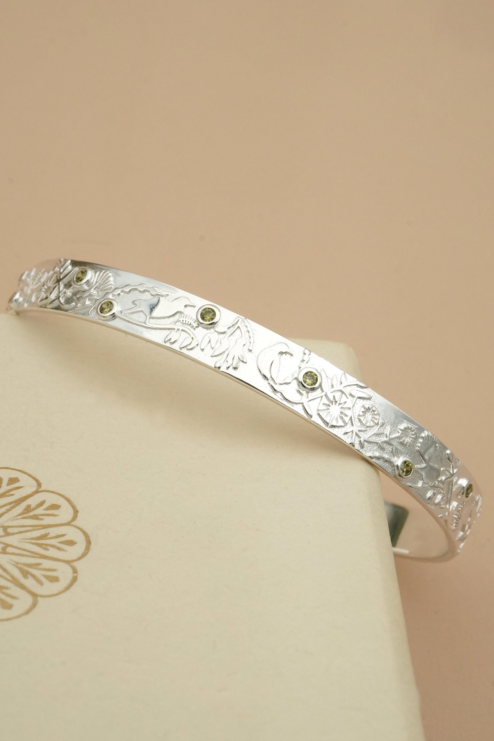 Silver cuff bracelet with NZ forest fauna patterns on a beige background