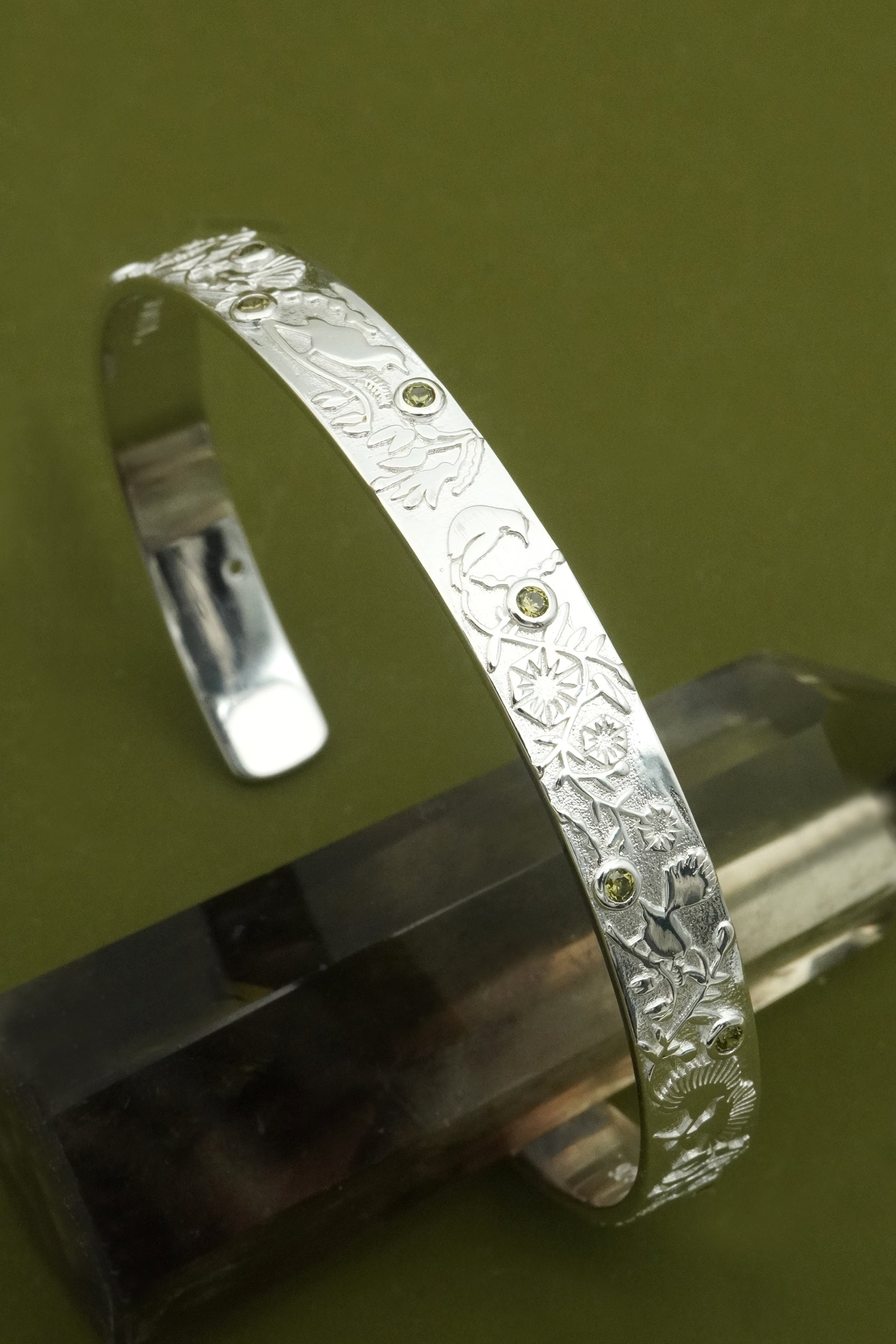 Silver cuff bracelet with textured design on a reflective surface