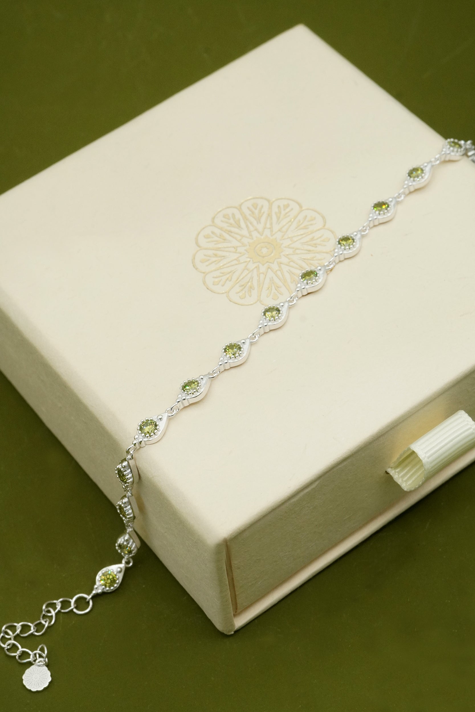 Silver elegant bracelet with olive green gemstones on a decorative box