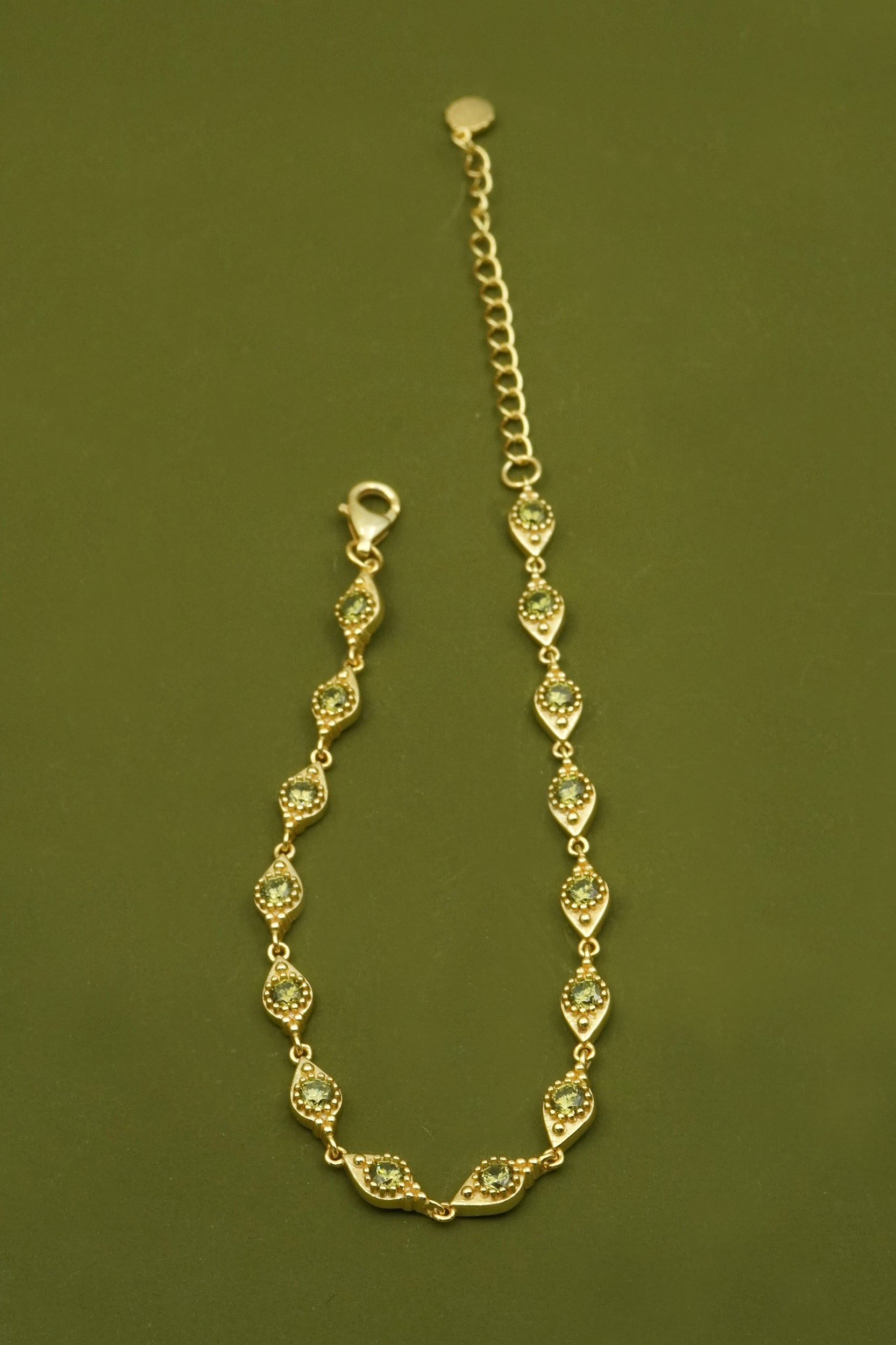 Gold filigree bracelet with green gemstones on a green background