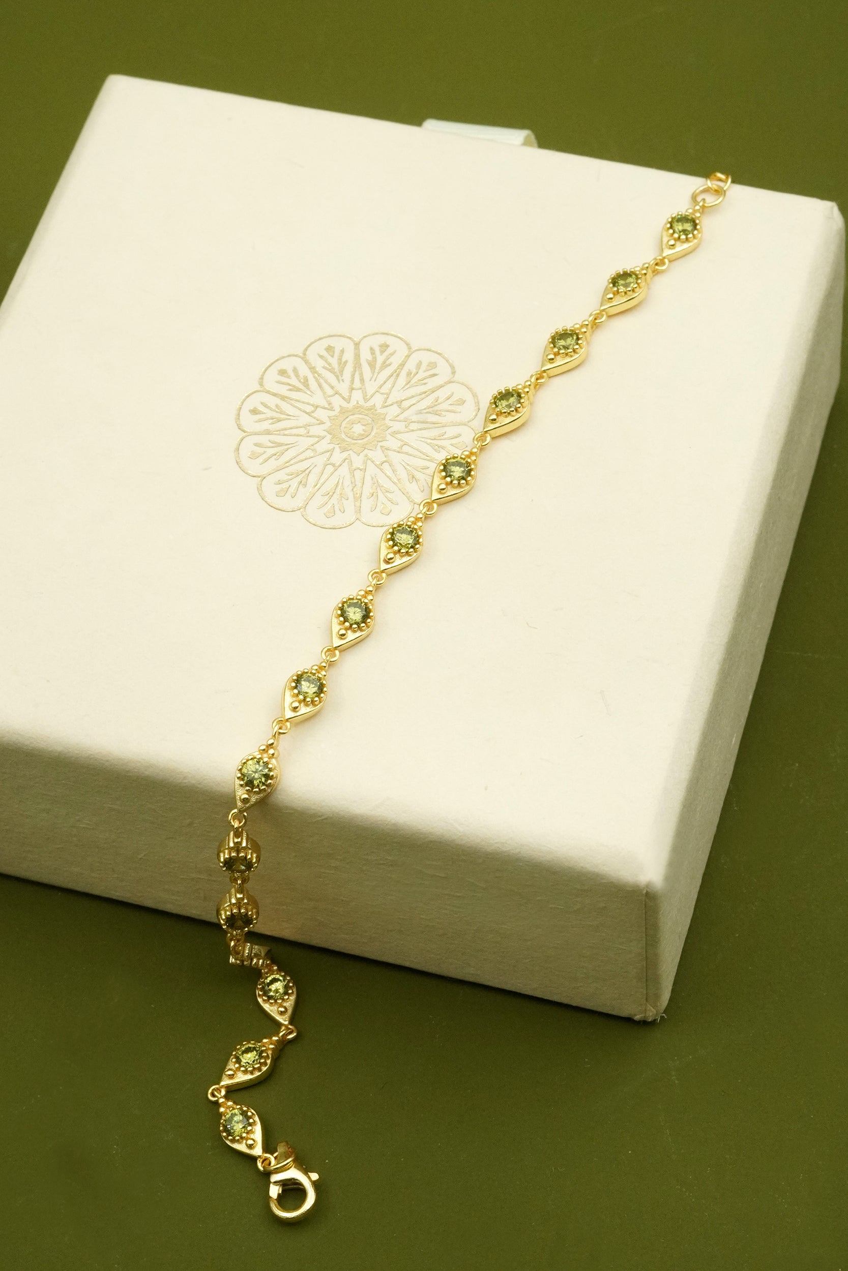 Gold bracelet on a white jewelry box with a green background