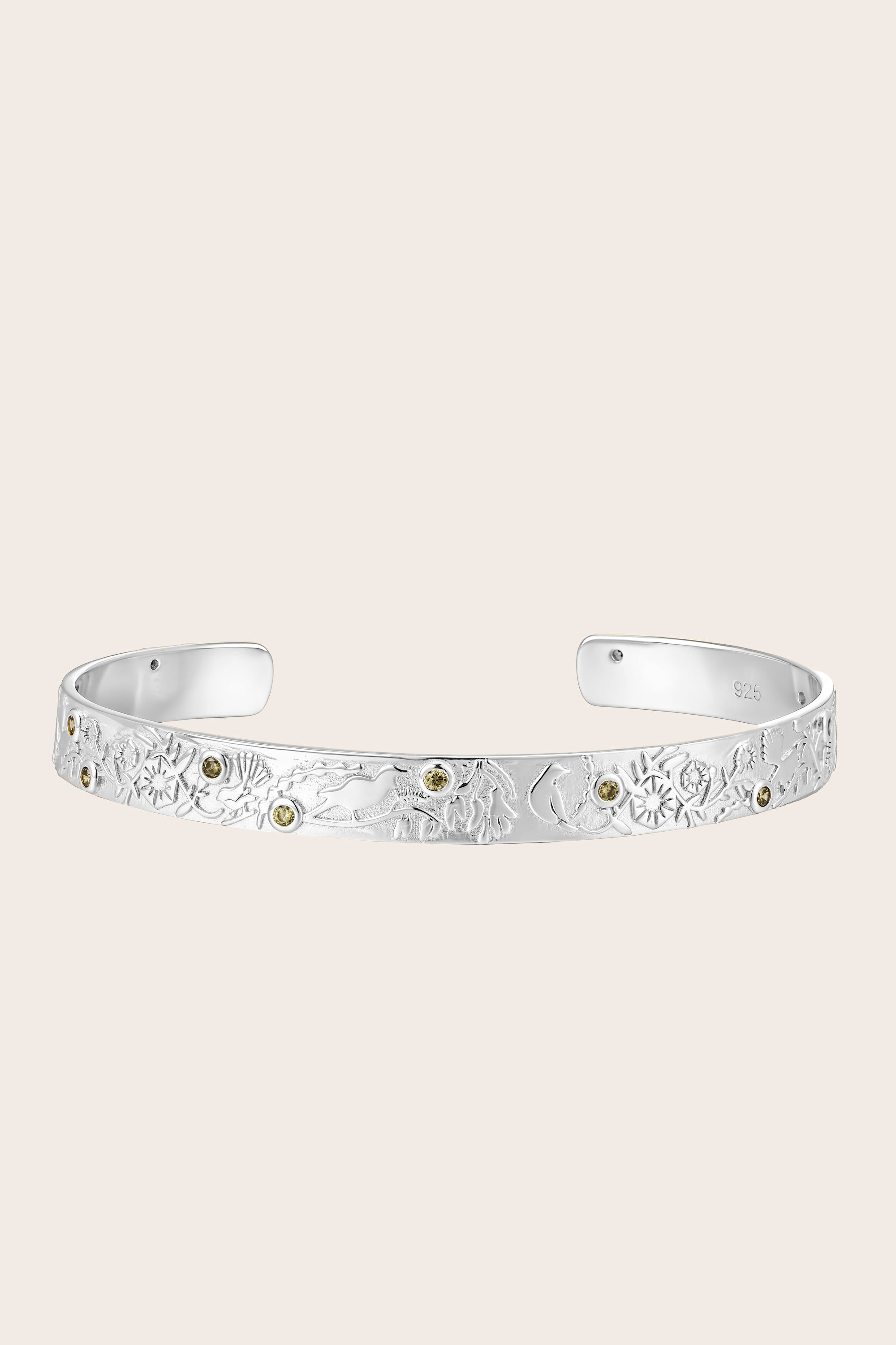 Silver cuff bracelet with floral forest design on a light beige background