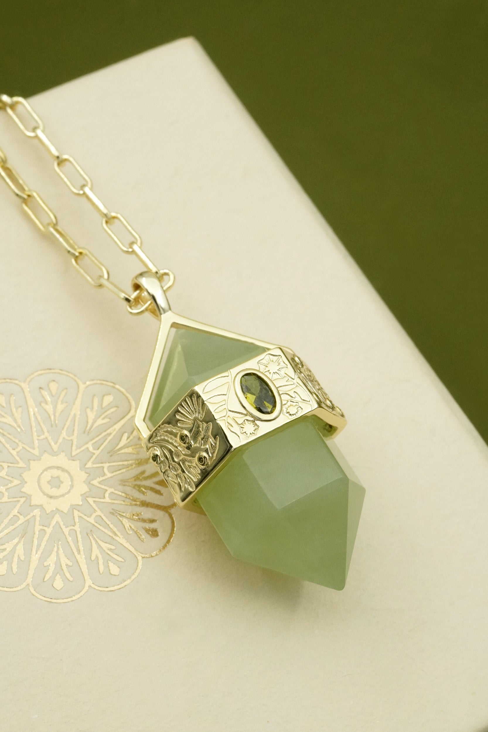 Necklace with a green floral pendant on a white surface with a gold chain.