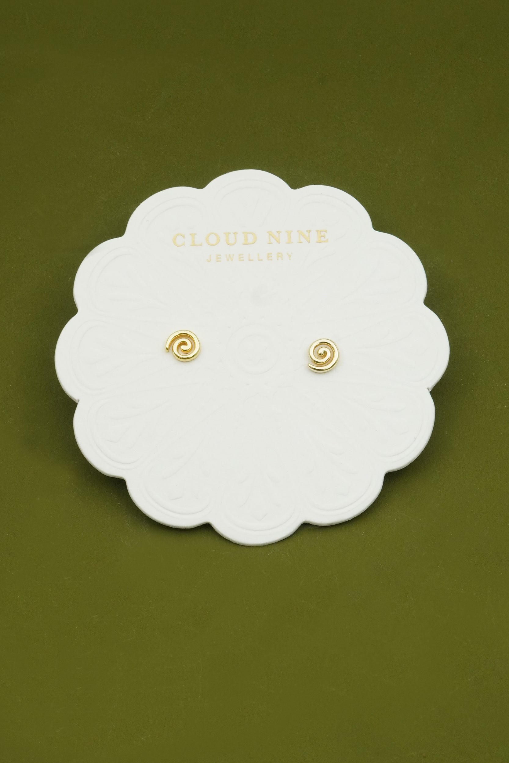 Gold spiral fern koru earrings on a white card with 'Cloud Nine Jewellery' branding against a green background
