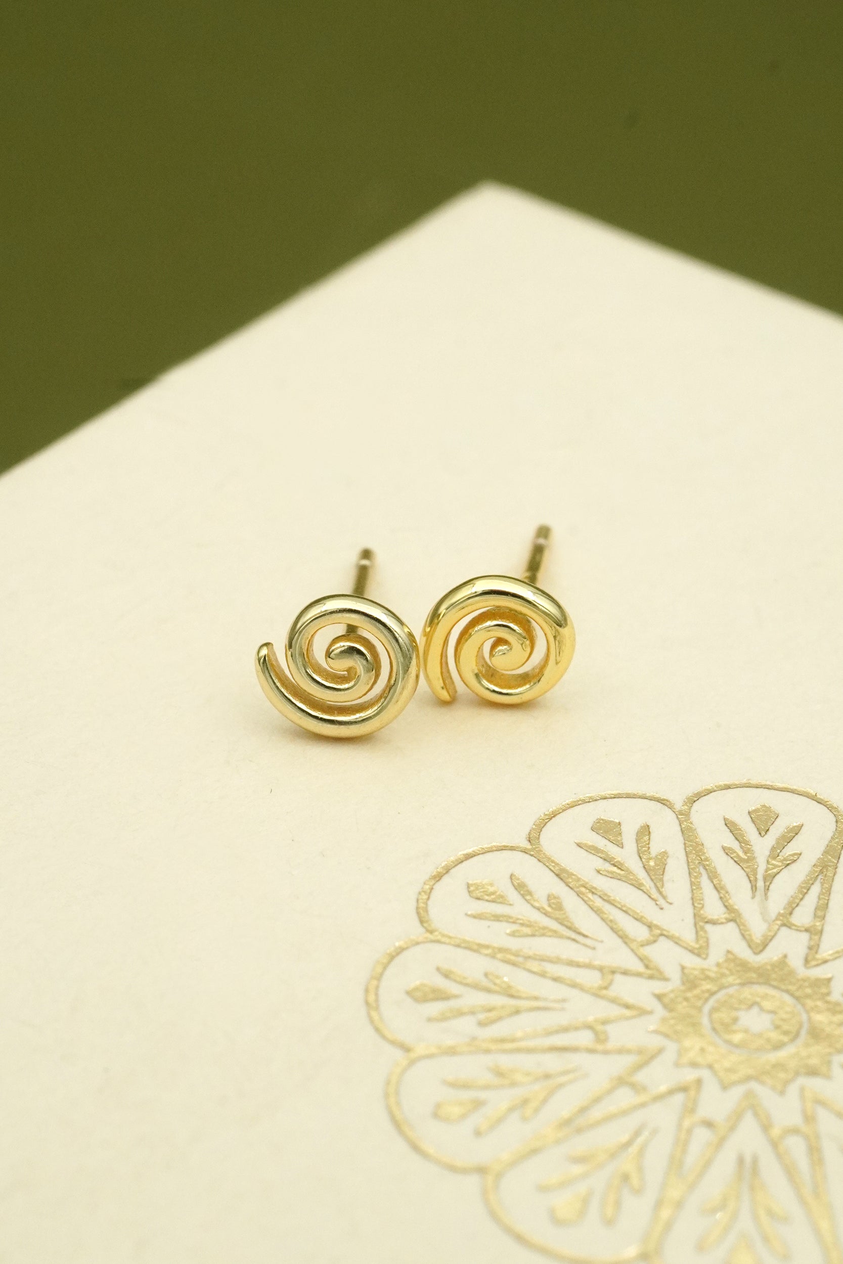 Gold koru stud earrings on cream box