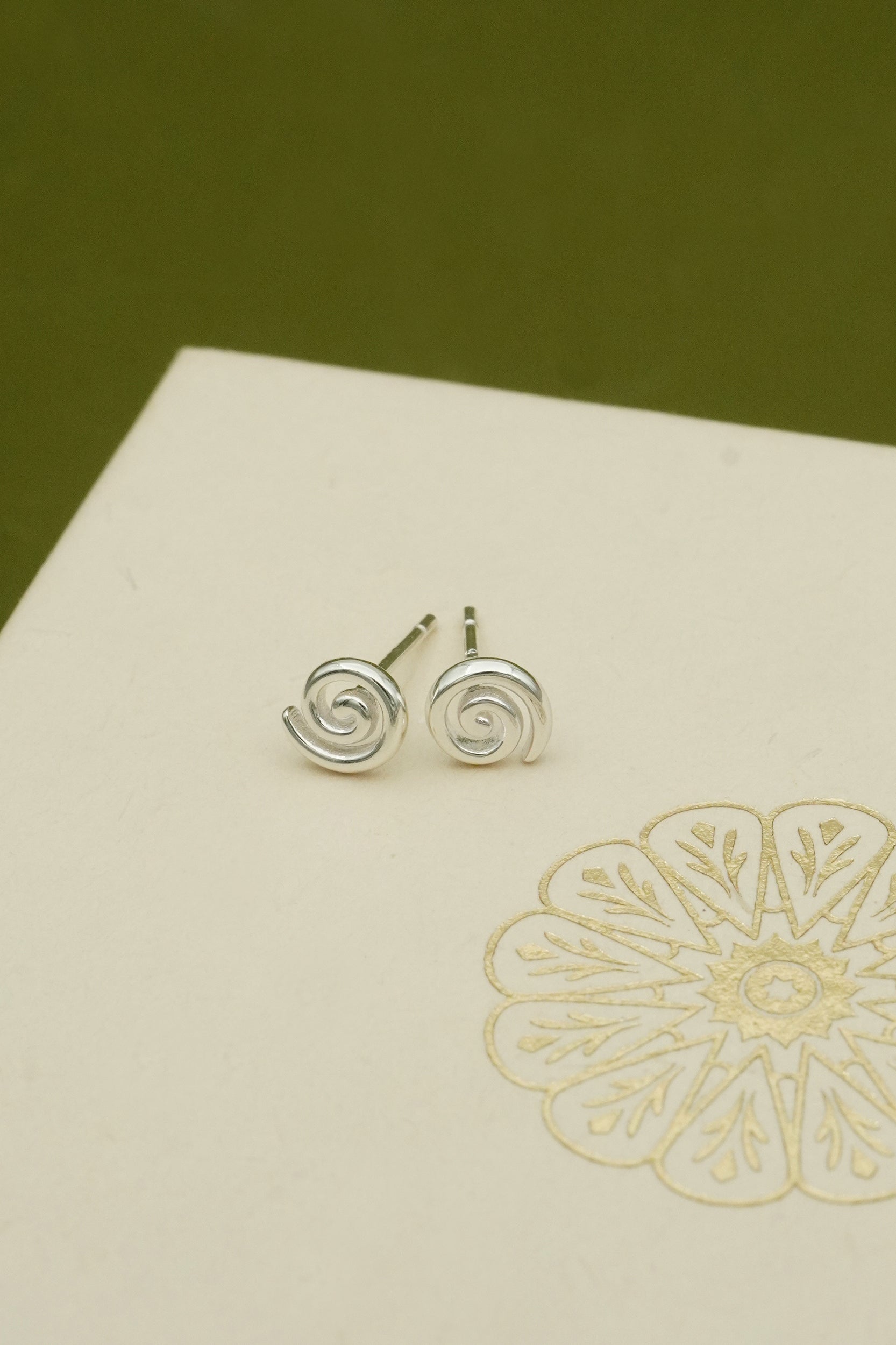 Silver spiral koru stud earrings on a beige card with floral design