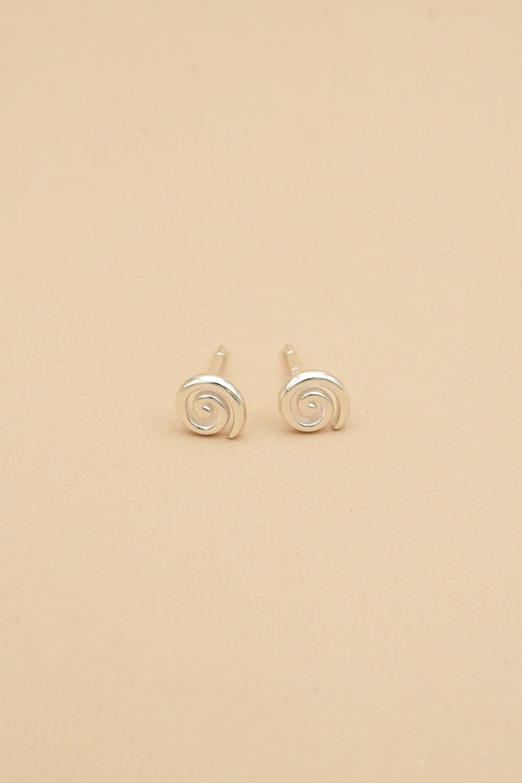 Pair of silver koru spiral earrings on a beige background