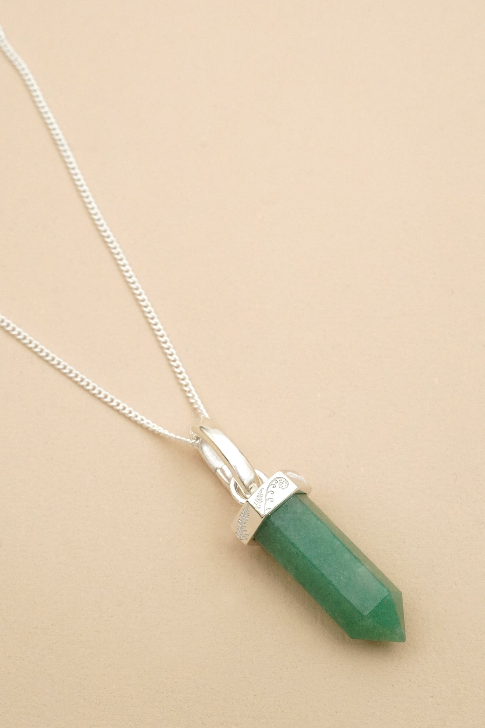 Necklace with a green aventurine crystal and NZ fern and koru detailing on a beige background