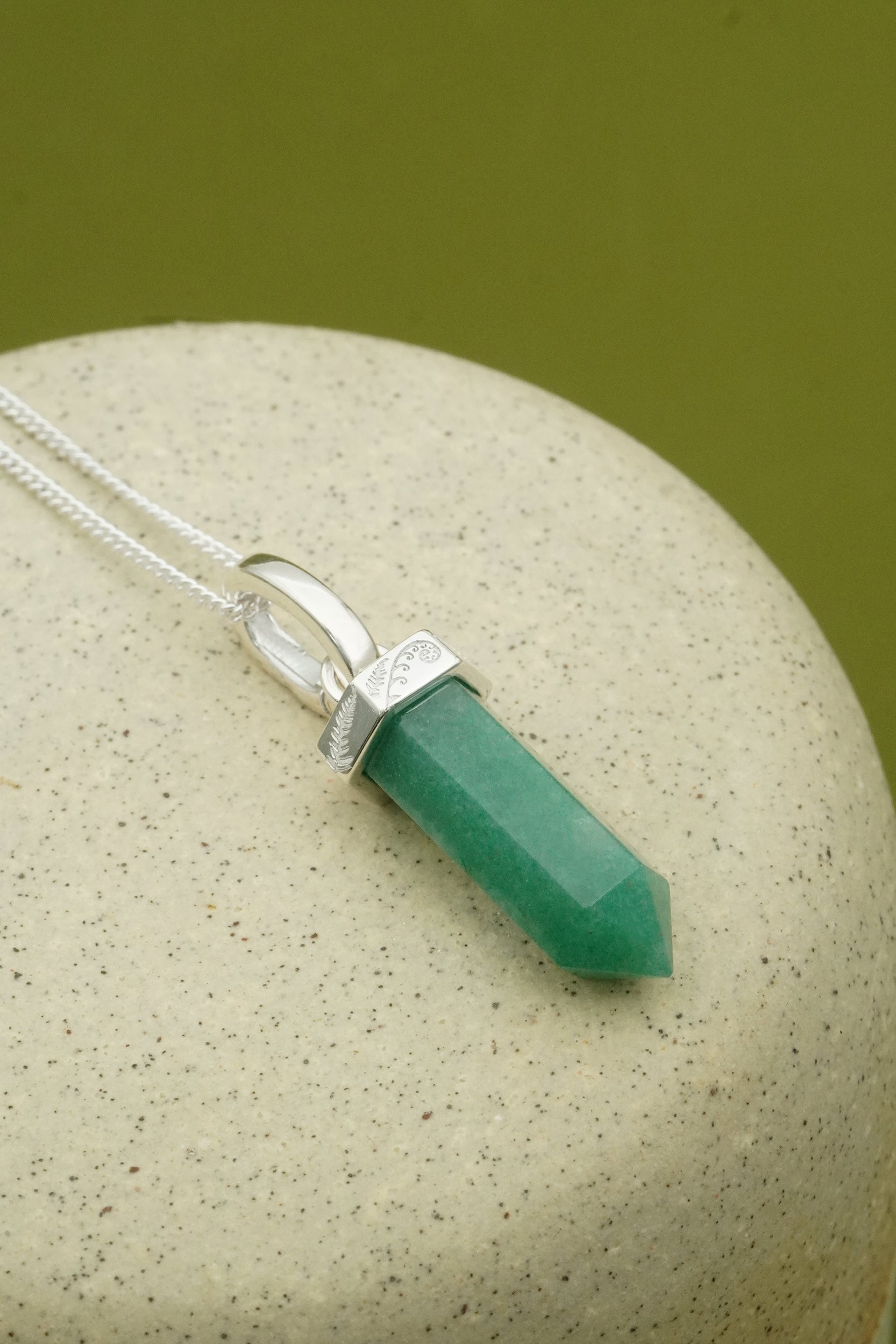 Green Aventurine crystal pendant on a silver chain against a beige stone background