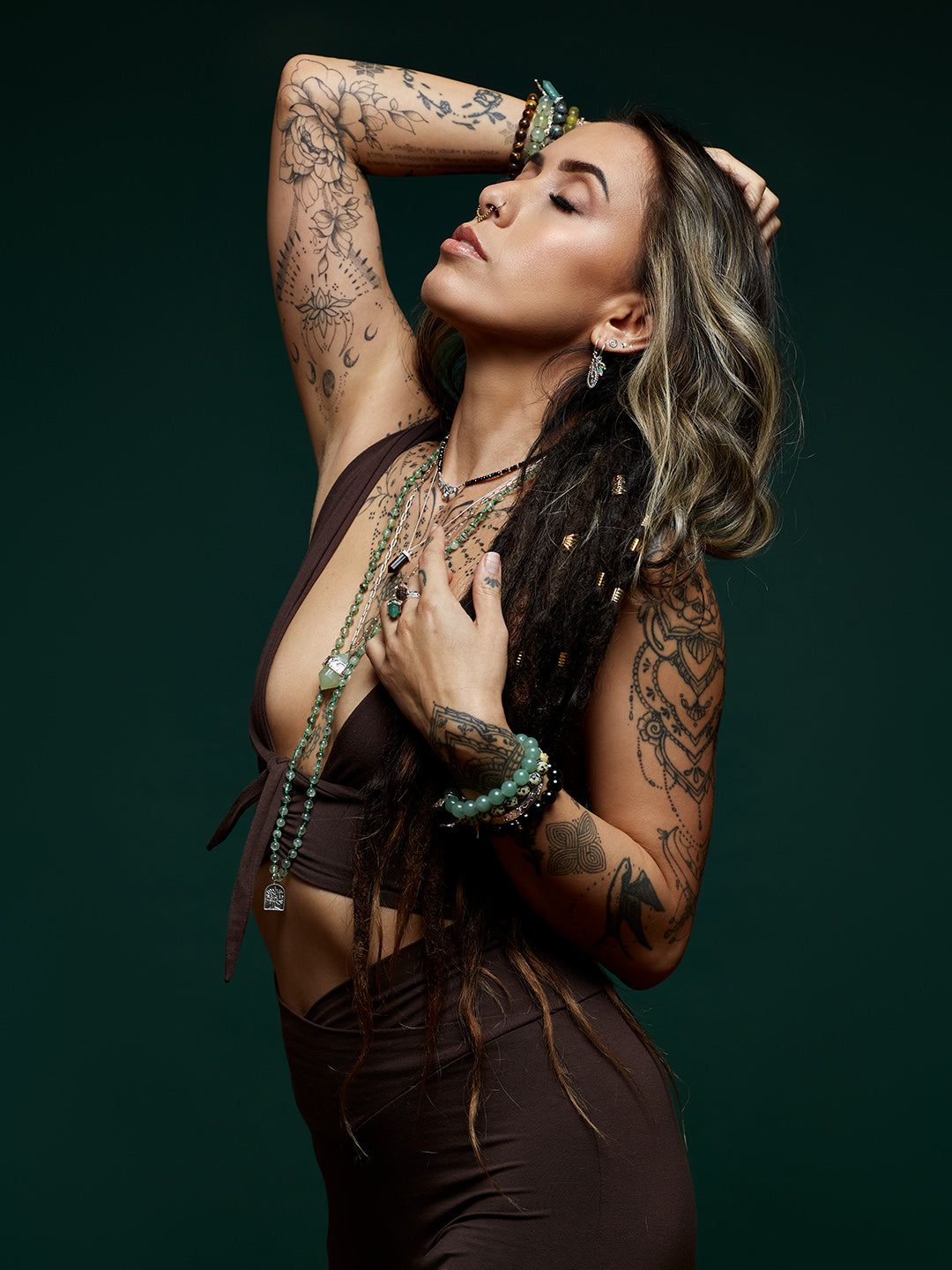 Woman with tattoos and spiritual jewellery against a dark background