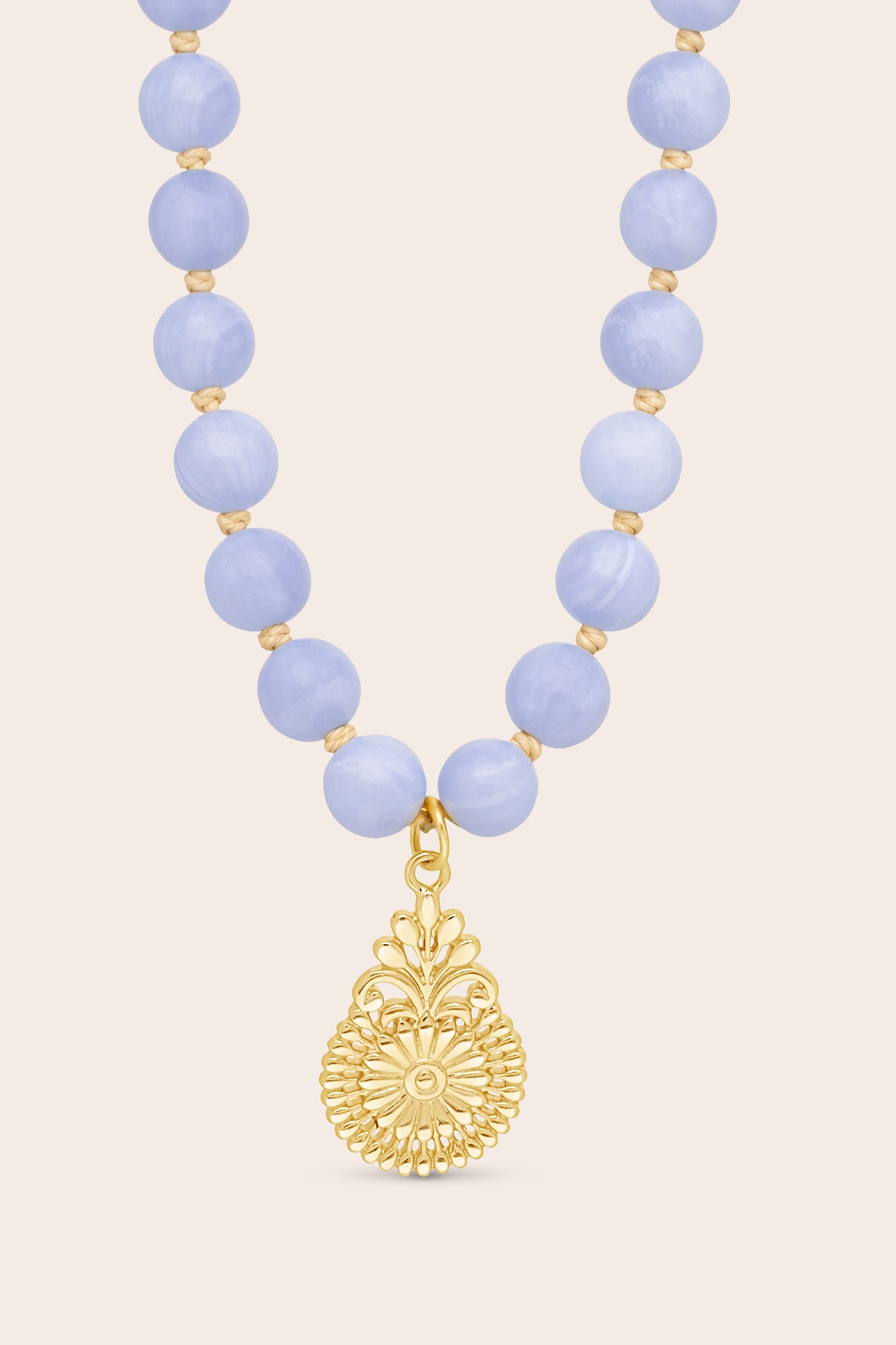 Necklace with blue beads and a gold pendant on a light pink background