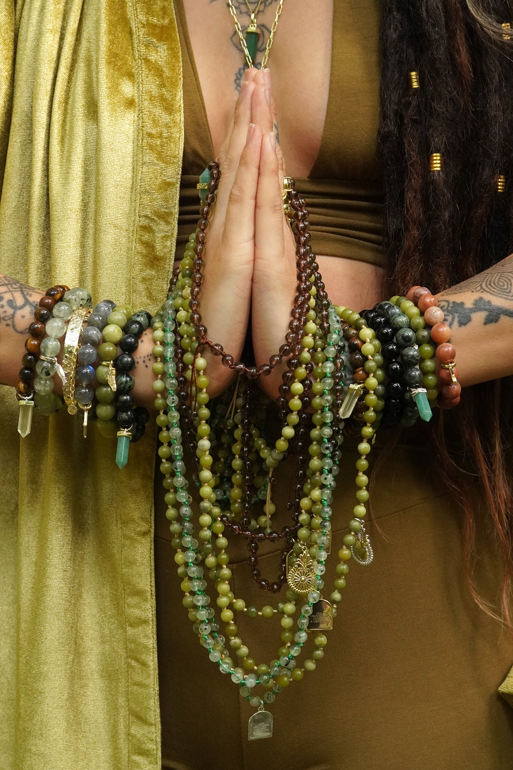 Person with multiple spiritual mala necklaces and bracelets, holding hands in prayer position.