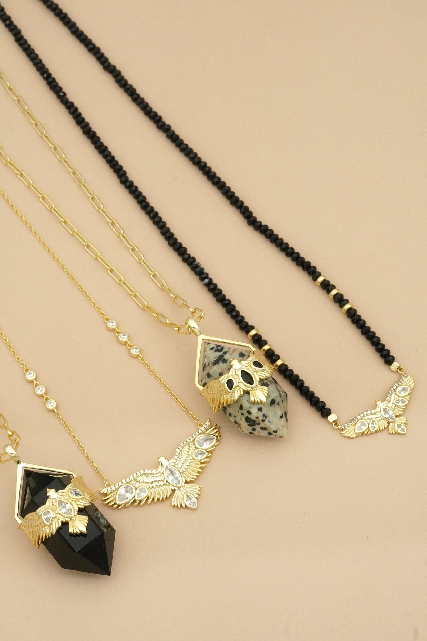 Four necklaces with black and gold soaring hawk pendants on a beige background