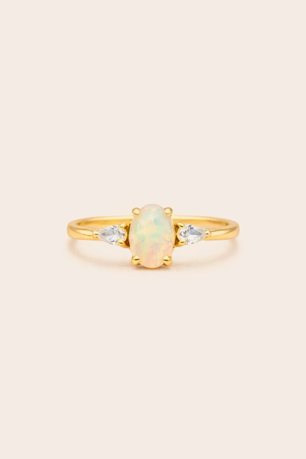 Gold ring with a central opal stone on a light beige background