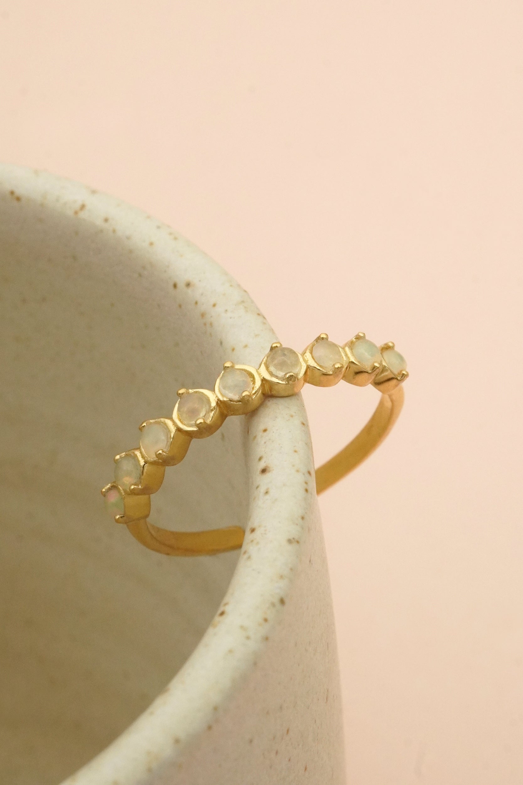 Gold ring with embedded opal stones on a ceramic mug against a pink background