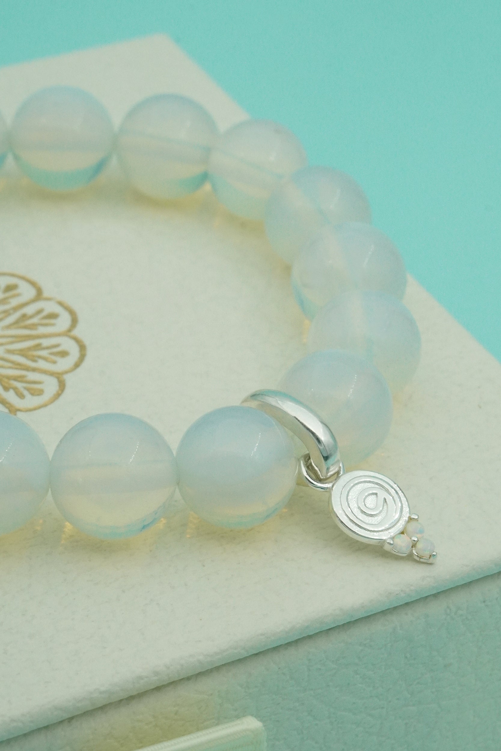 Opal beaded bracelet with a silver charm on a light turquoise background