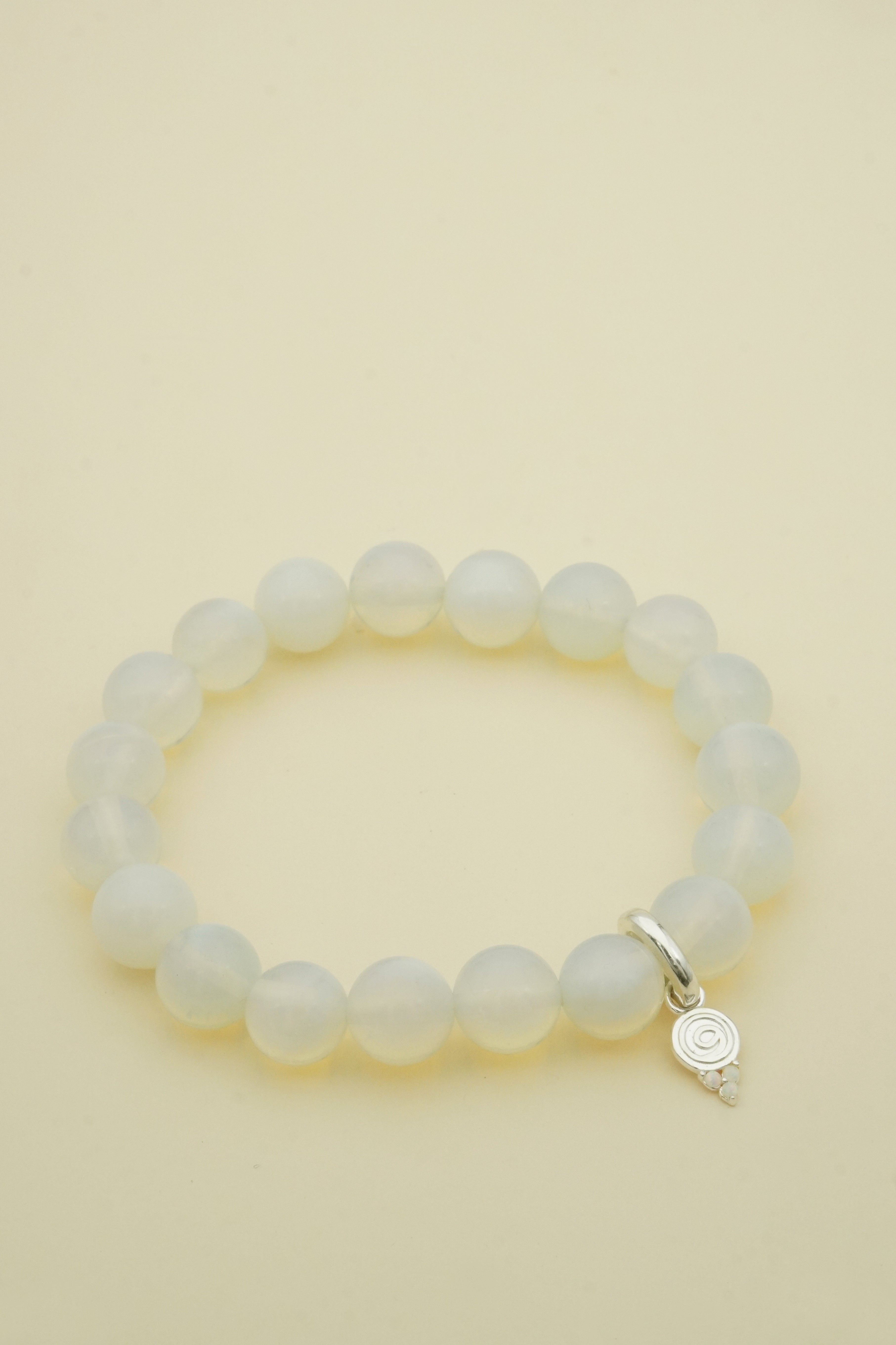 opal Beaded bracelet with a silver charm on a beige background