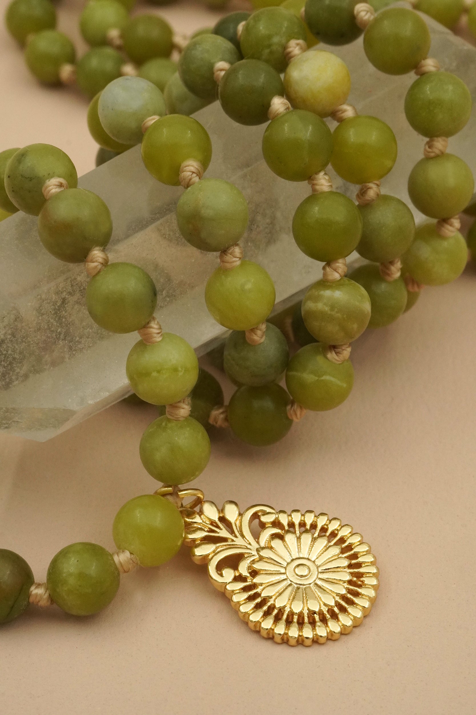Green beaded male necklace with a gold flower pendant on a beige surface