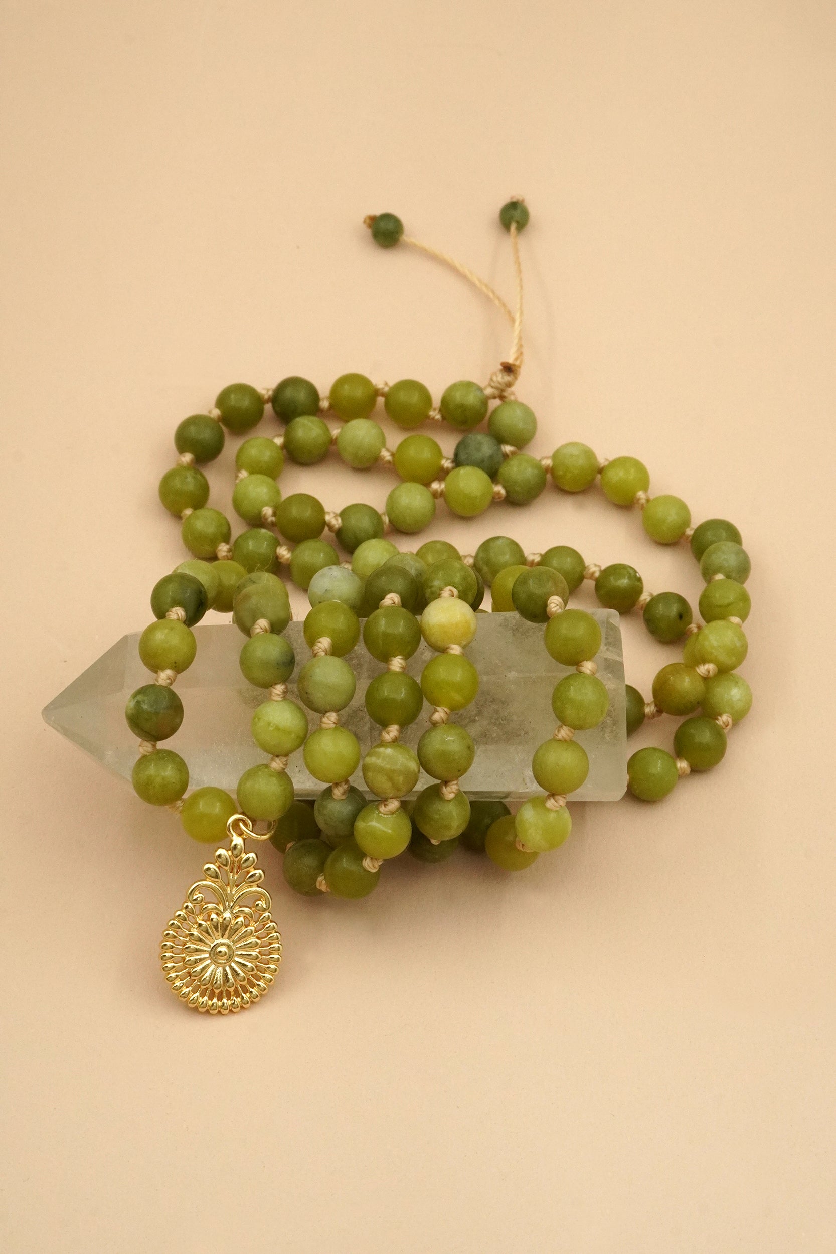 Green beaded mala prayer necklace with a gold pendant on a beige background