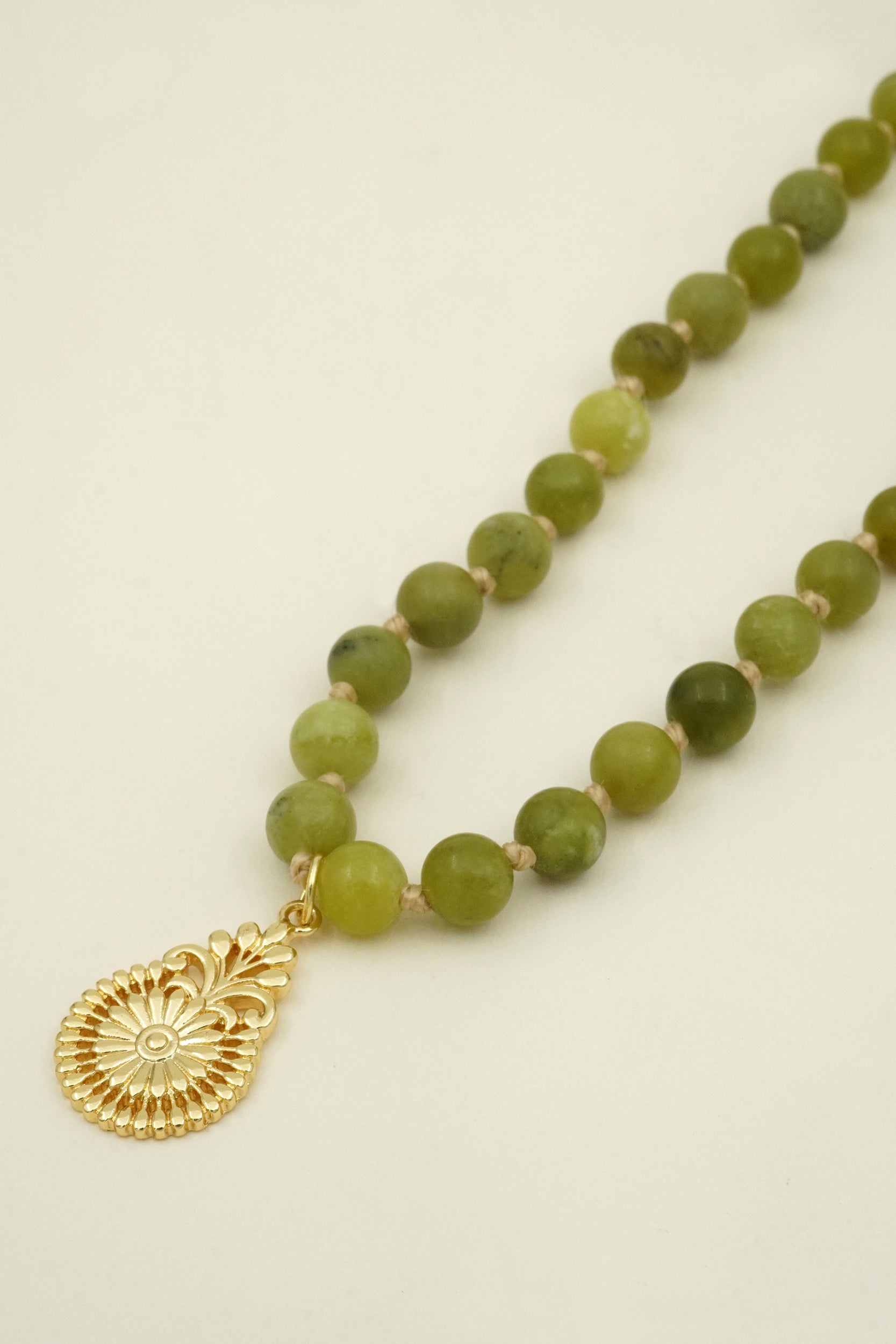 Green beaded spiritual mala prayer necklace with a gold pendant on a beige background