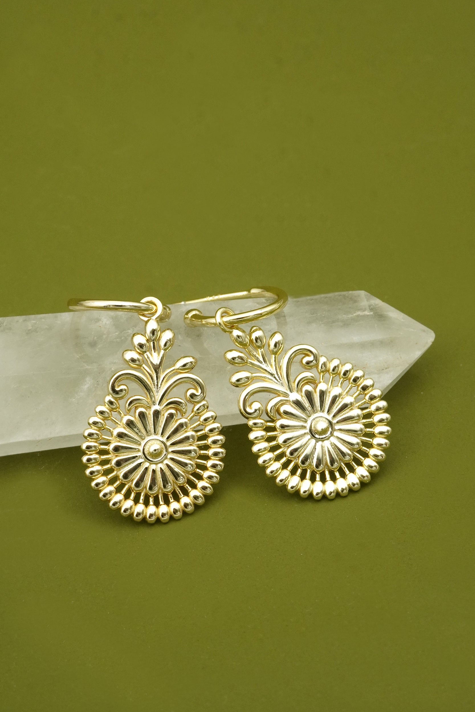 Gold paisley filigree flower earrings with intricate designs on a green background