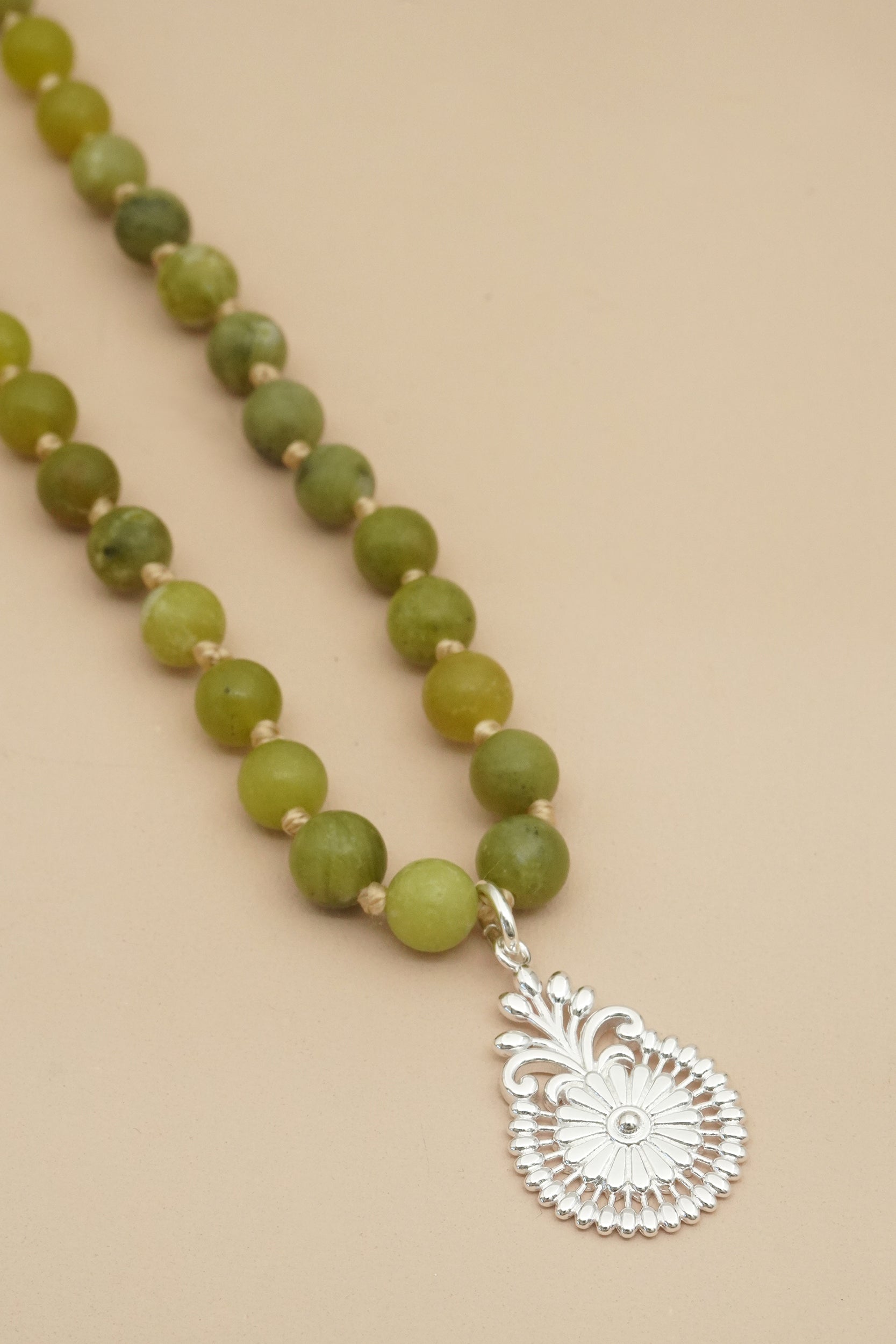 Necklace with green beads and a silver pendant on a beige background
