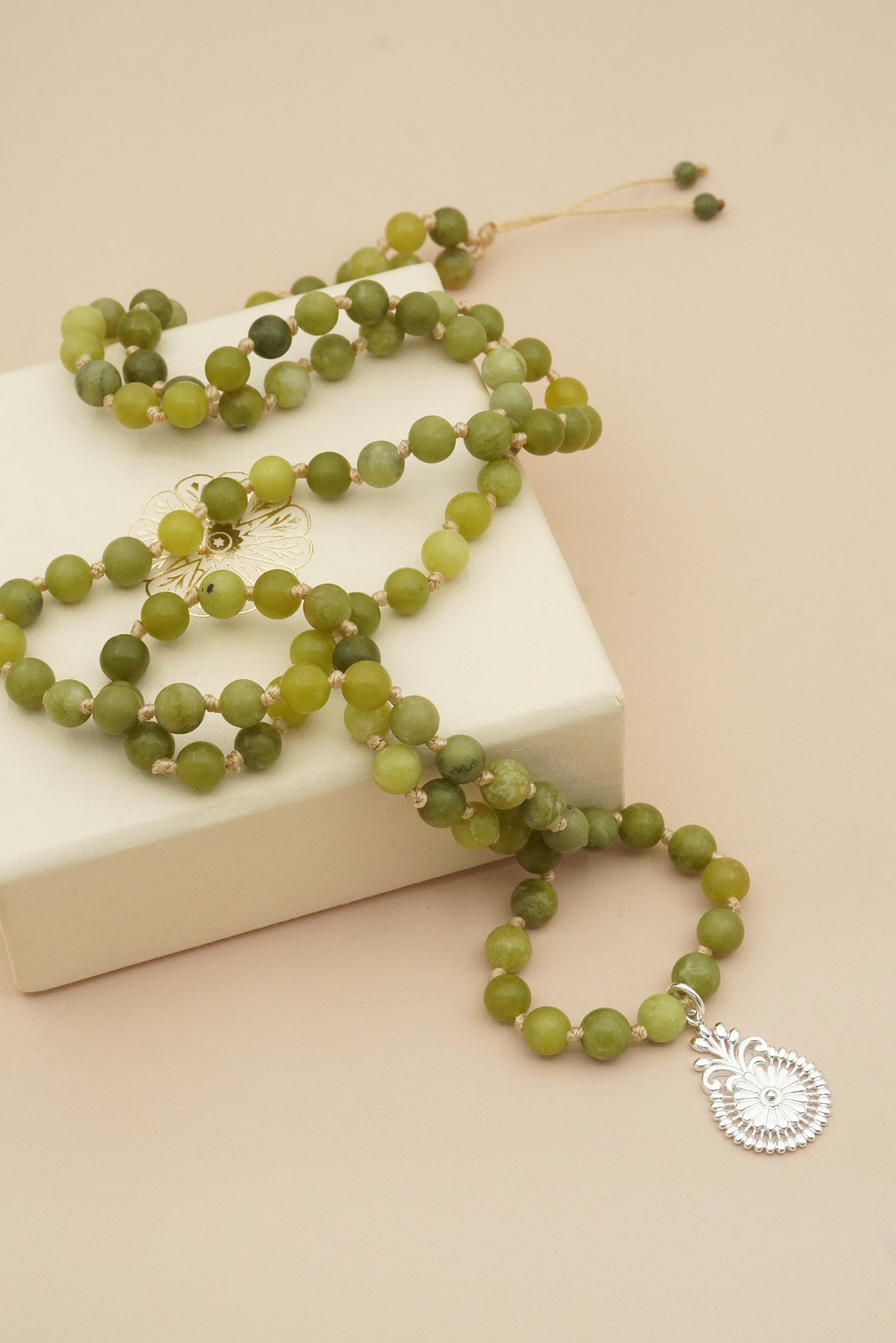 Green beaded male prayer necklace with a silver pendant on a beige surface