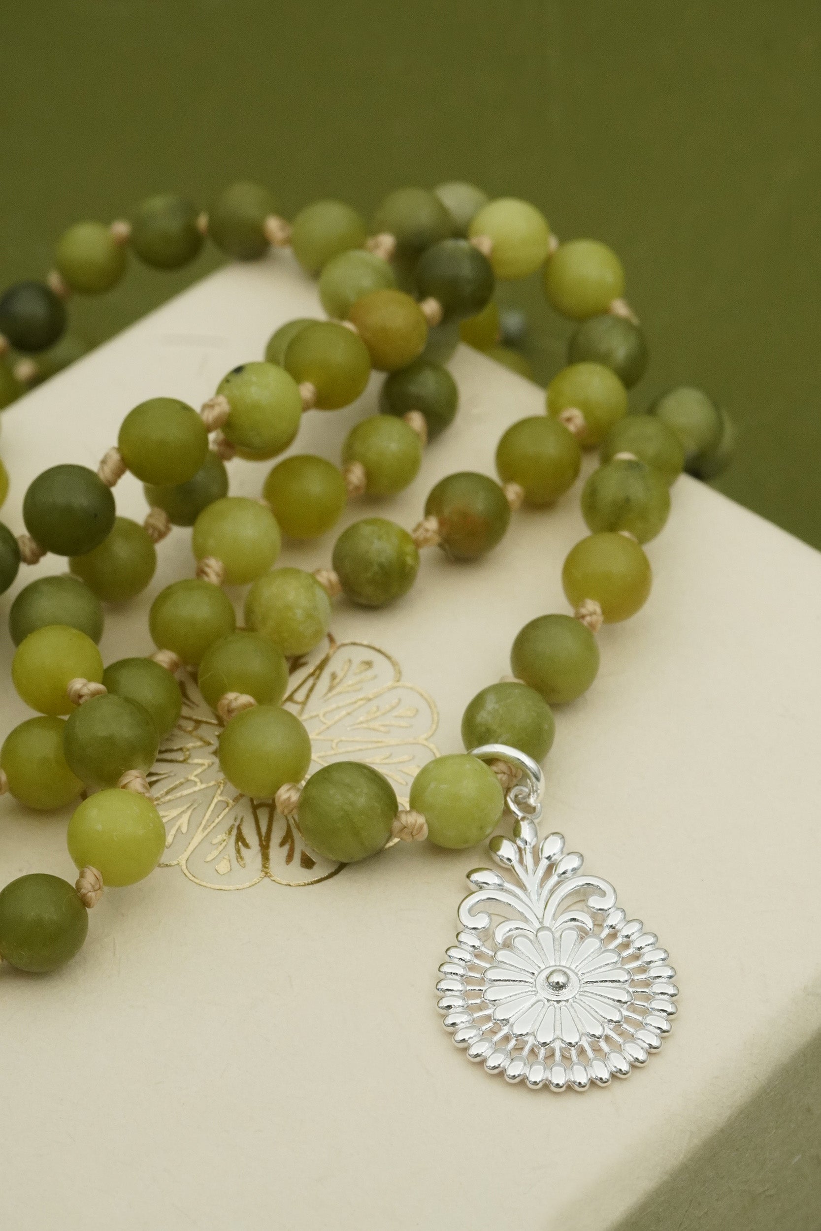 Green beaded mala prayer necklace with a silver pendant on a white surface