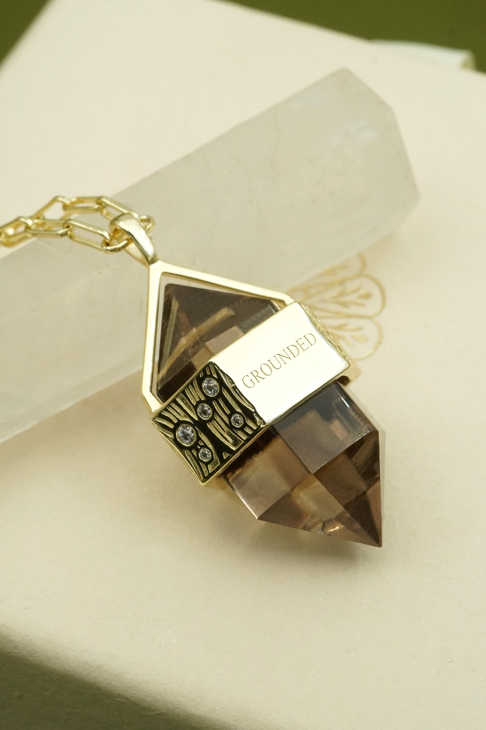 Gold crystal necklace with a faceted smoky quartz brown pendant inscribed with grounded on a white surface