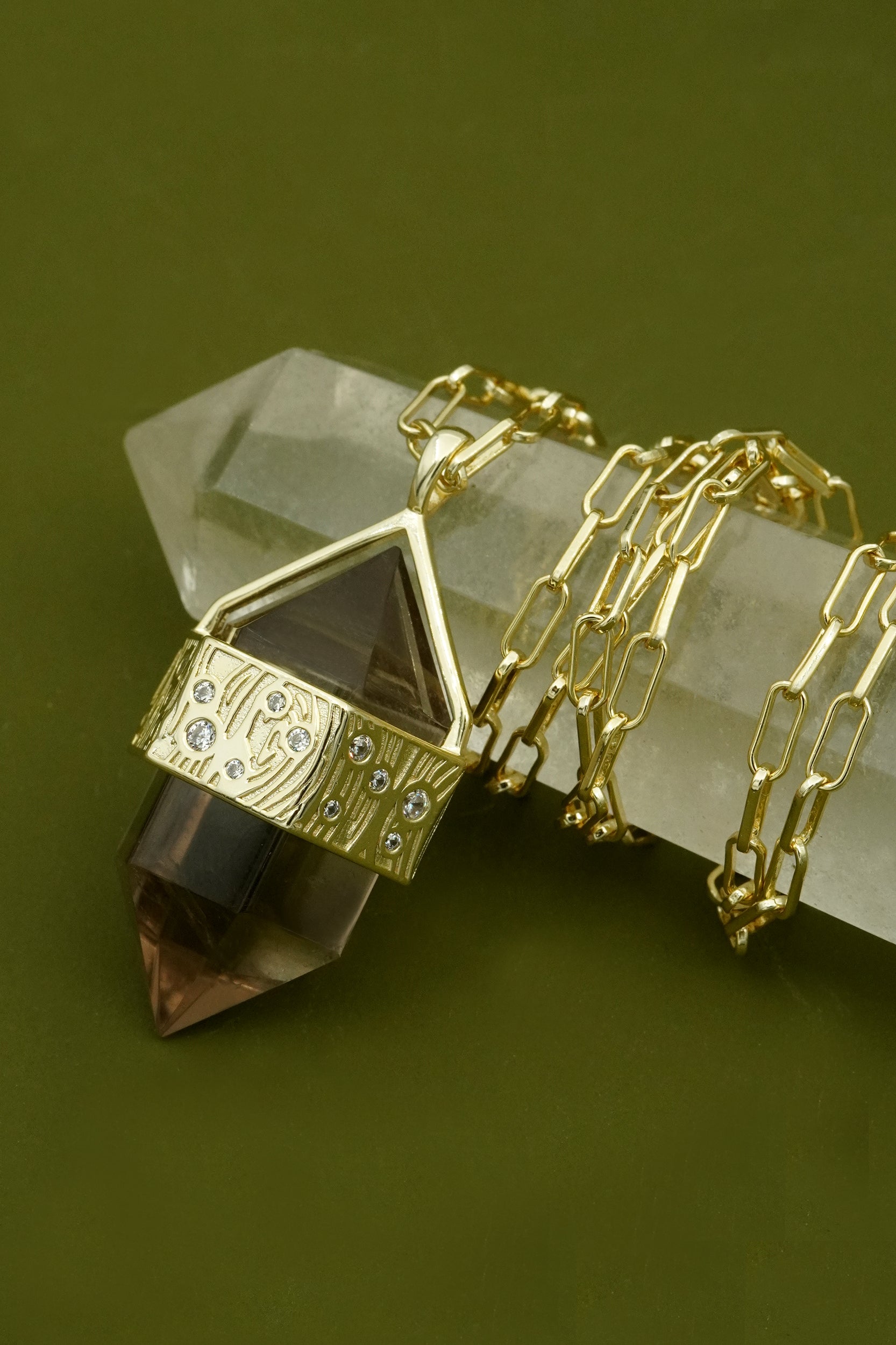 Gold crystal necklace with a grounded pendant on a green background