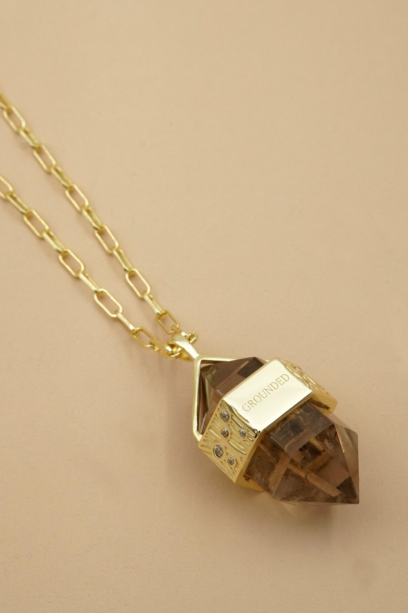 Gold necklace with a grounded nature inspired pendant on a beige background