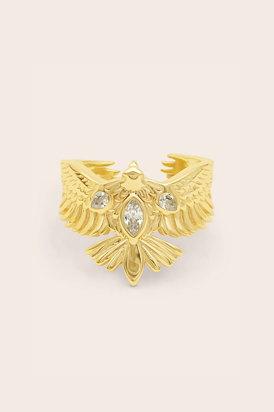 Gold ring with eagle soar design on a beige background