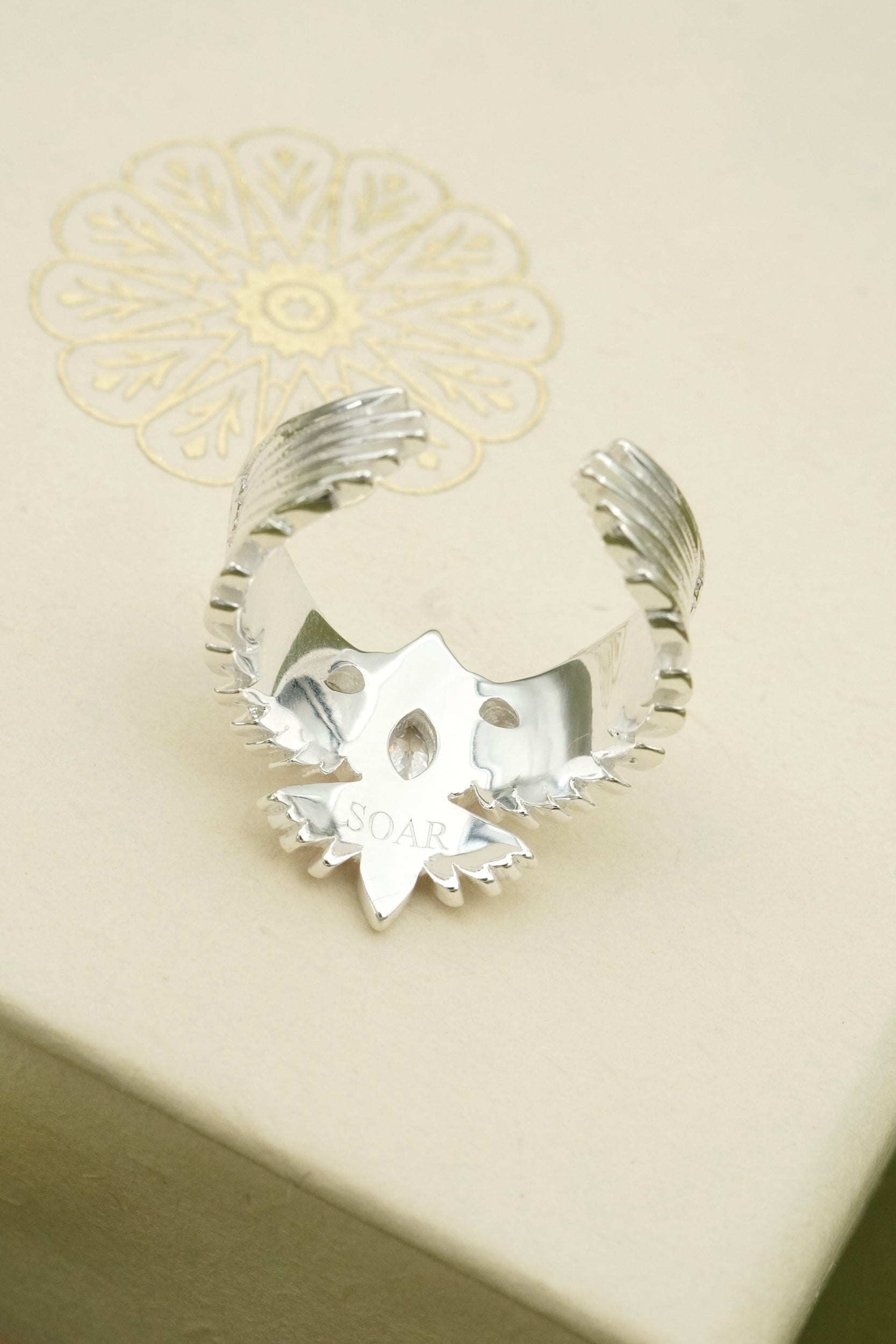 Silver ring with a unique design and words SOAR engraved on inside of ring band on a beige background