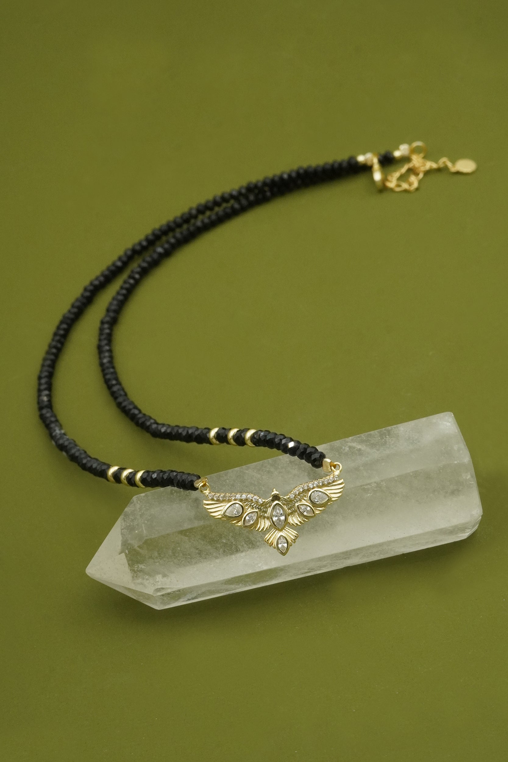 Necklace with black agate beads and gold accents on a crystal point against a green background