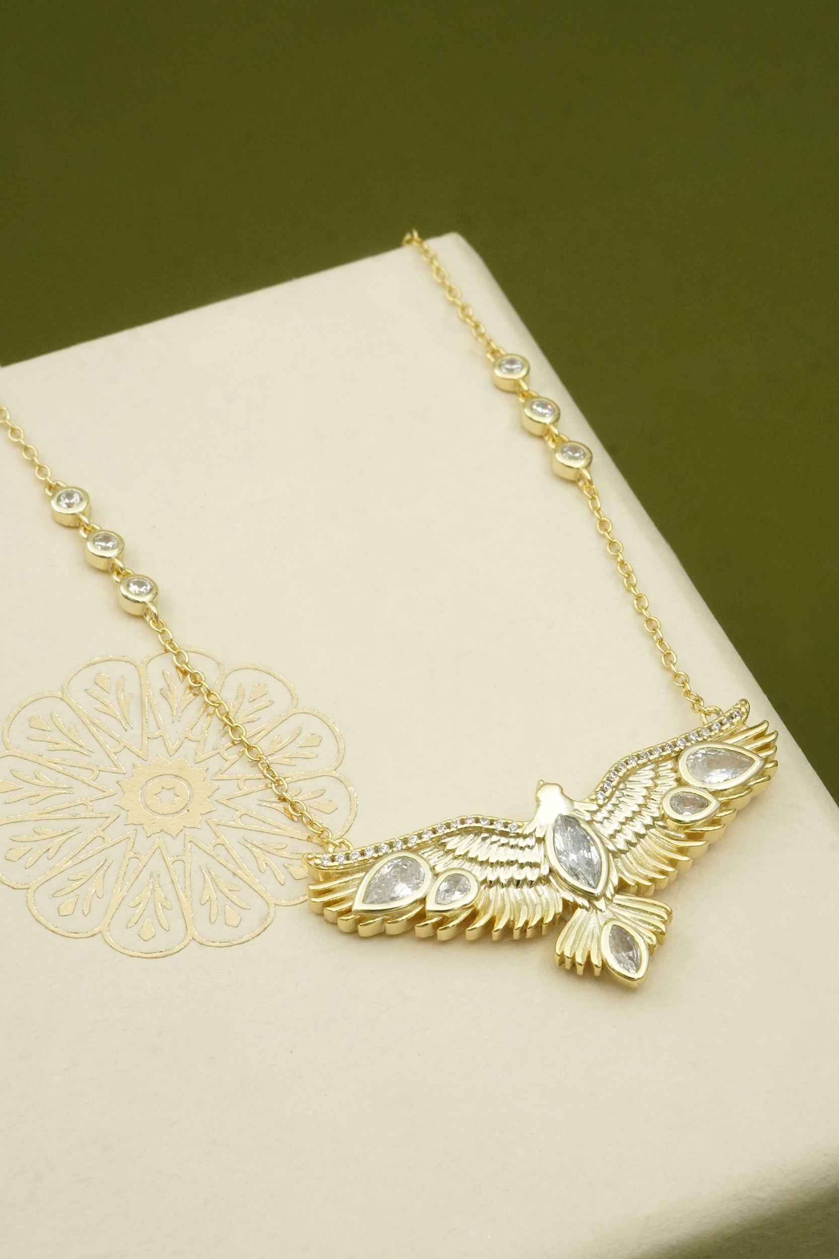 Gold necklace with a hawk bird on a beige surface