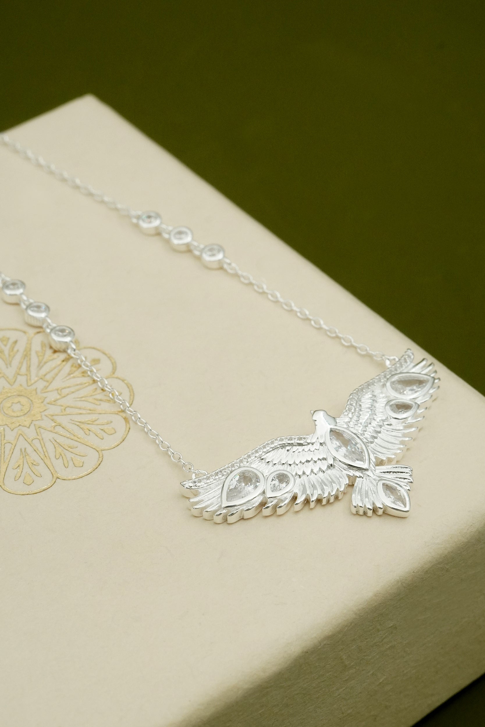Silver soaring hawk bird necklace with an intricate design on a beige box. 