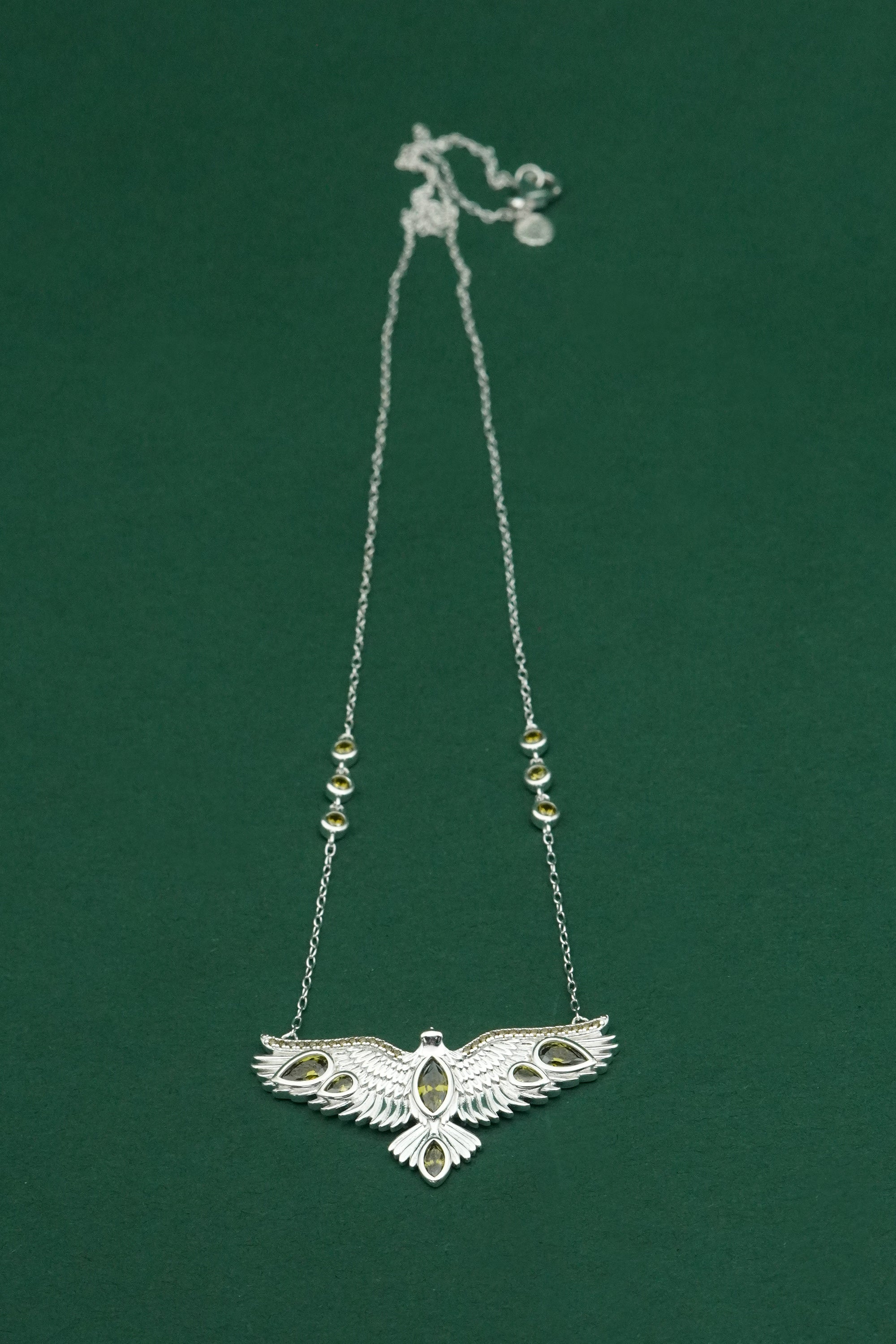 Silver necklace with an intricate wings open bird pendant on a green background