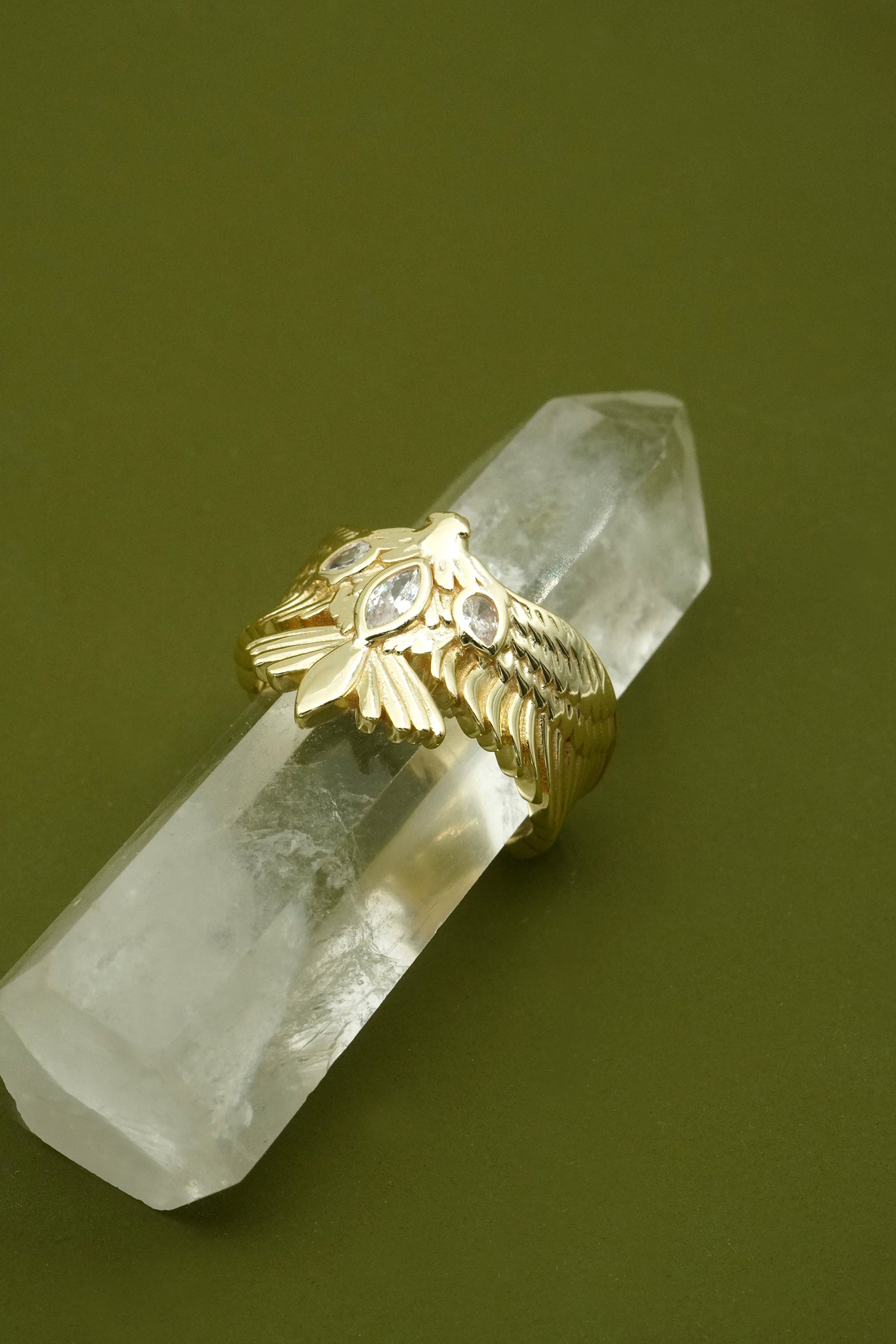 Gold eagle ring with hawk bird design on a crystal against a green background