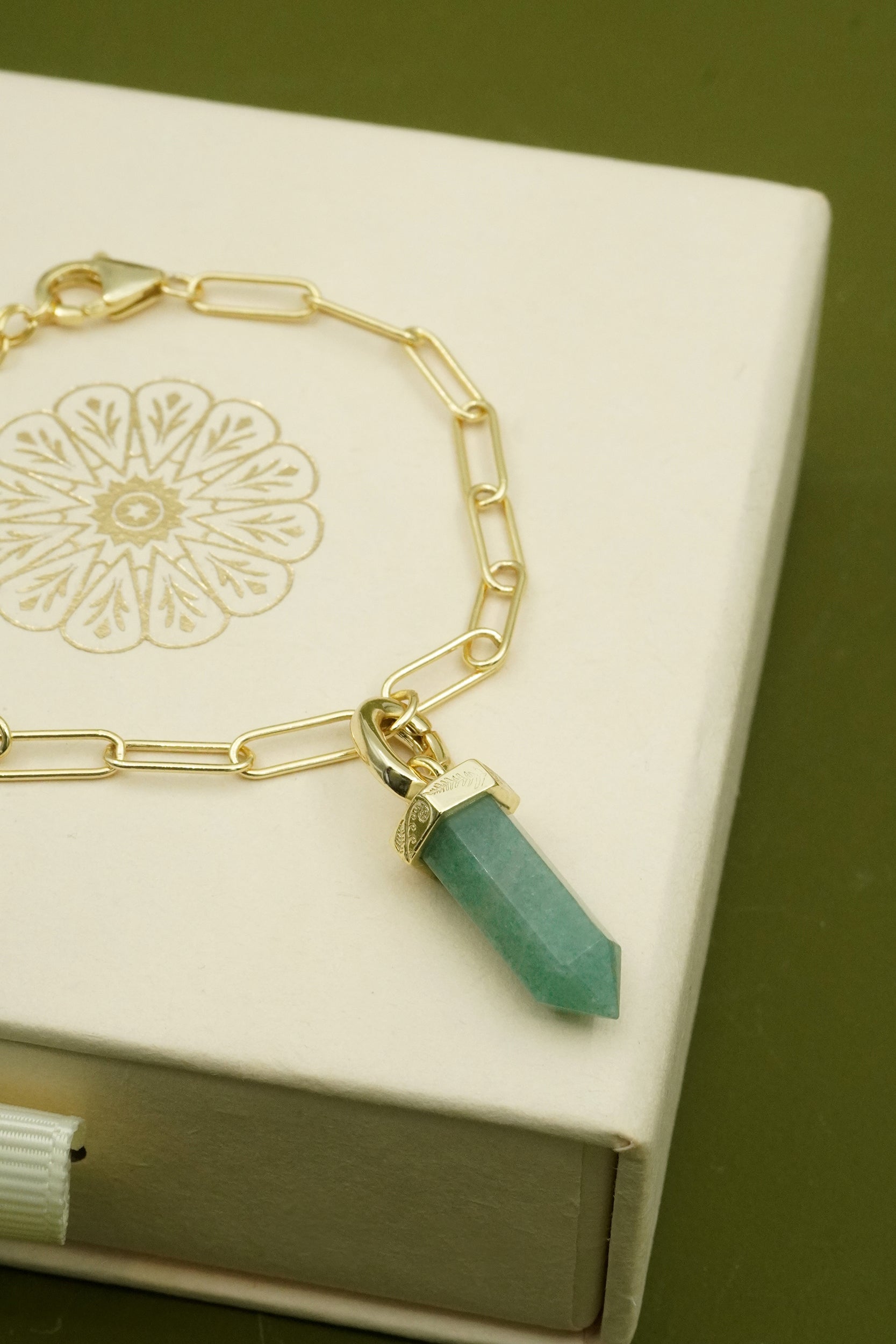 Gold bracelet with a green gemstone for grounding and strength charm on a decorative box