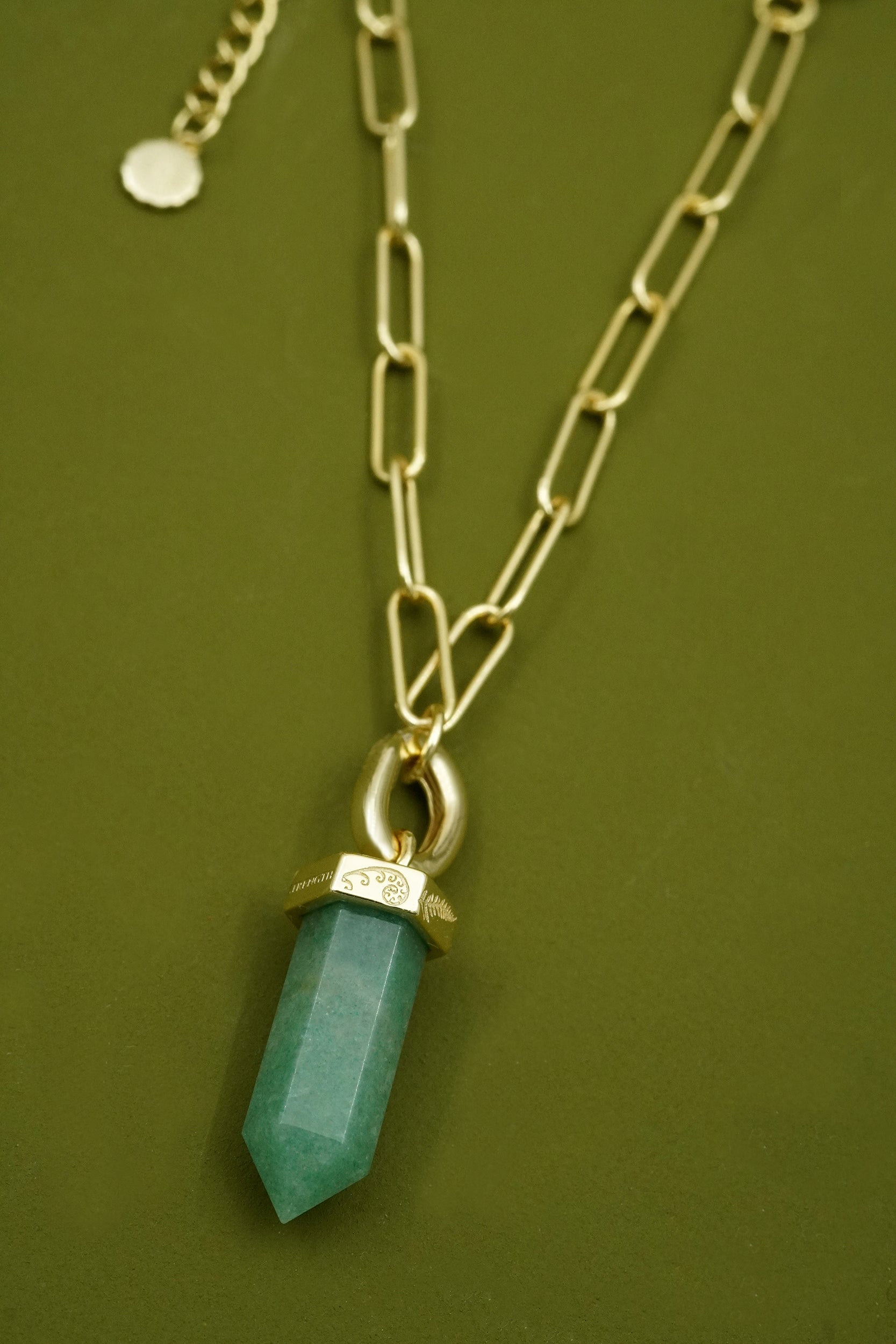 gold bracelet with a green aventurine gemstone pendant with koru and fern detailing against a green background