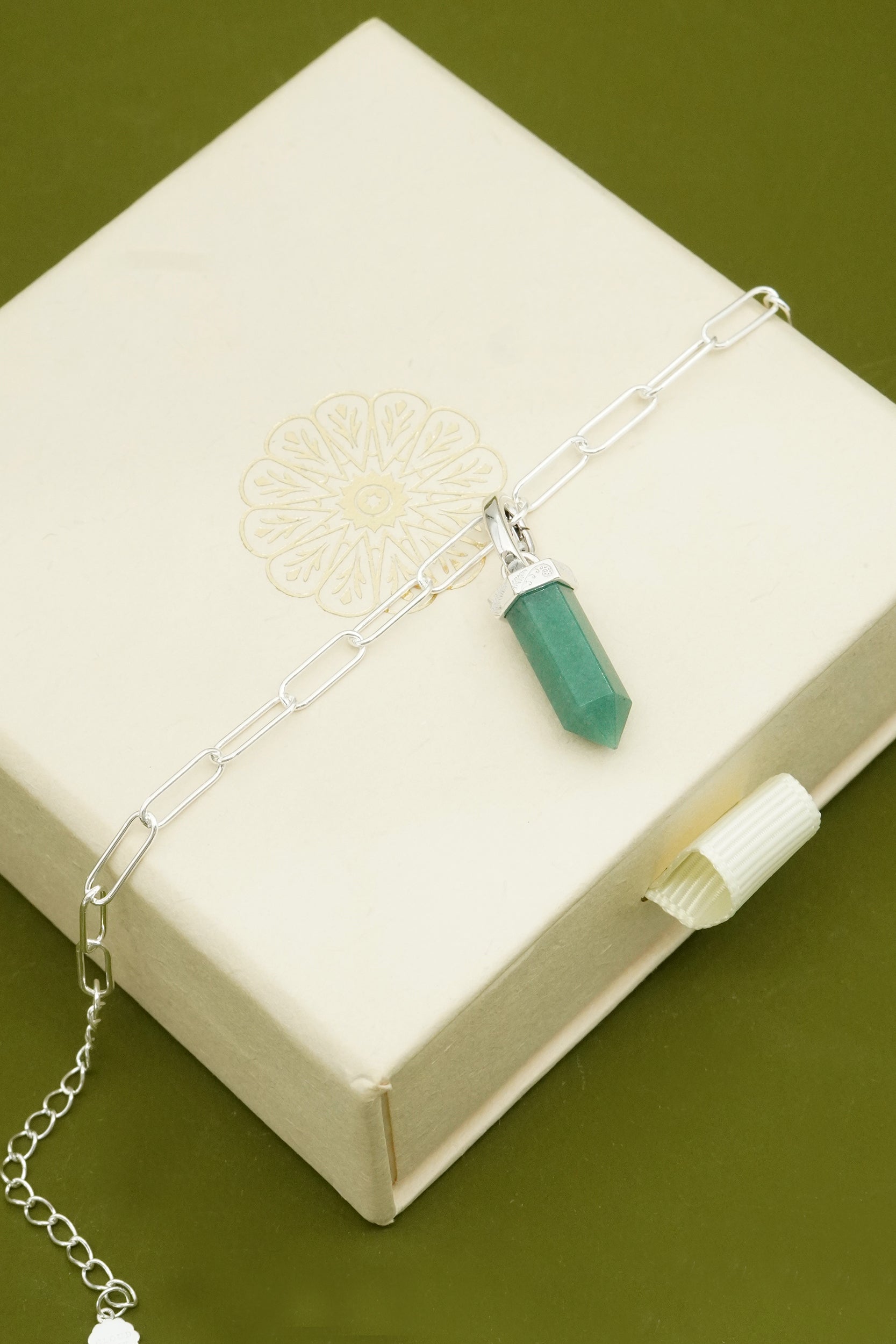 Necklace with a green aventurine pendant on a white box against a green background