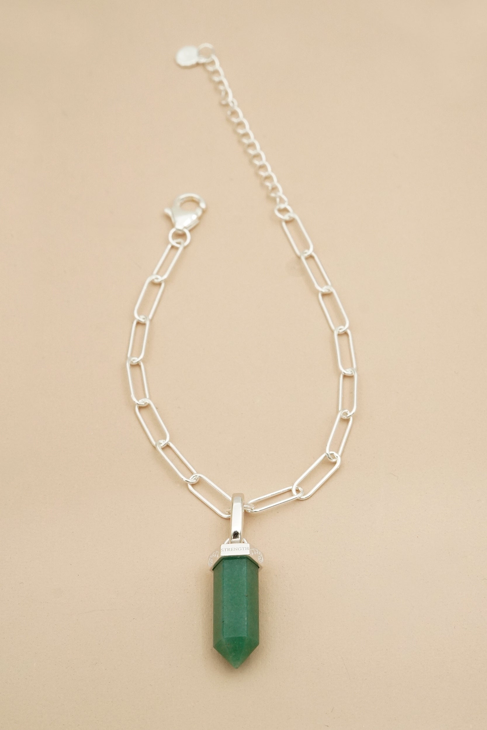 Silver chain necklace with a green pendant on a beige background