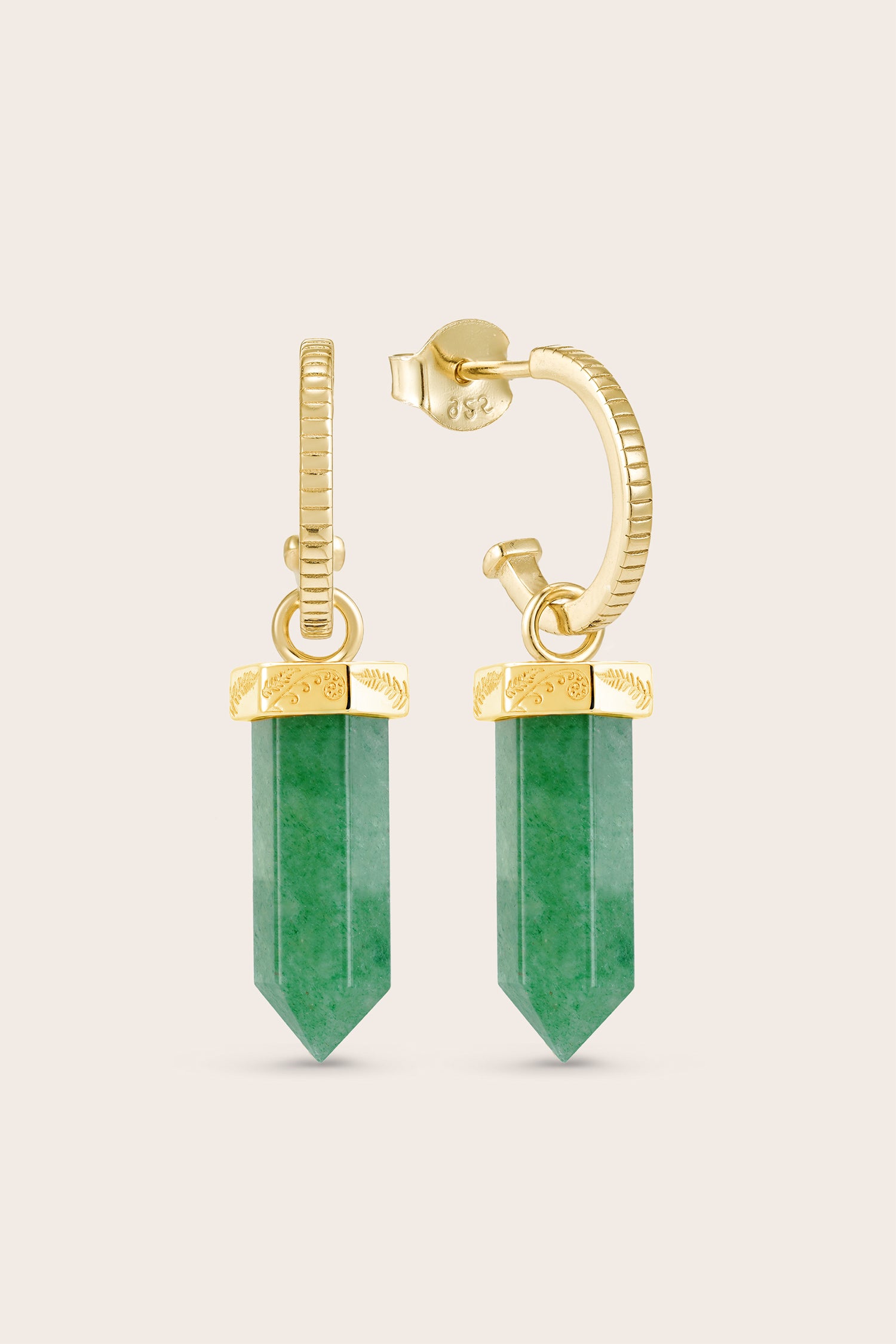 Gold earrings with green gemstones on a beige background