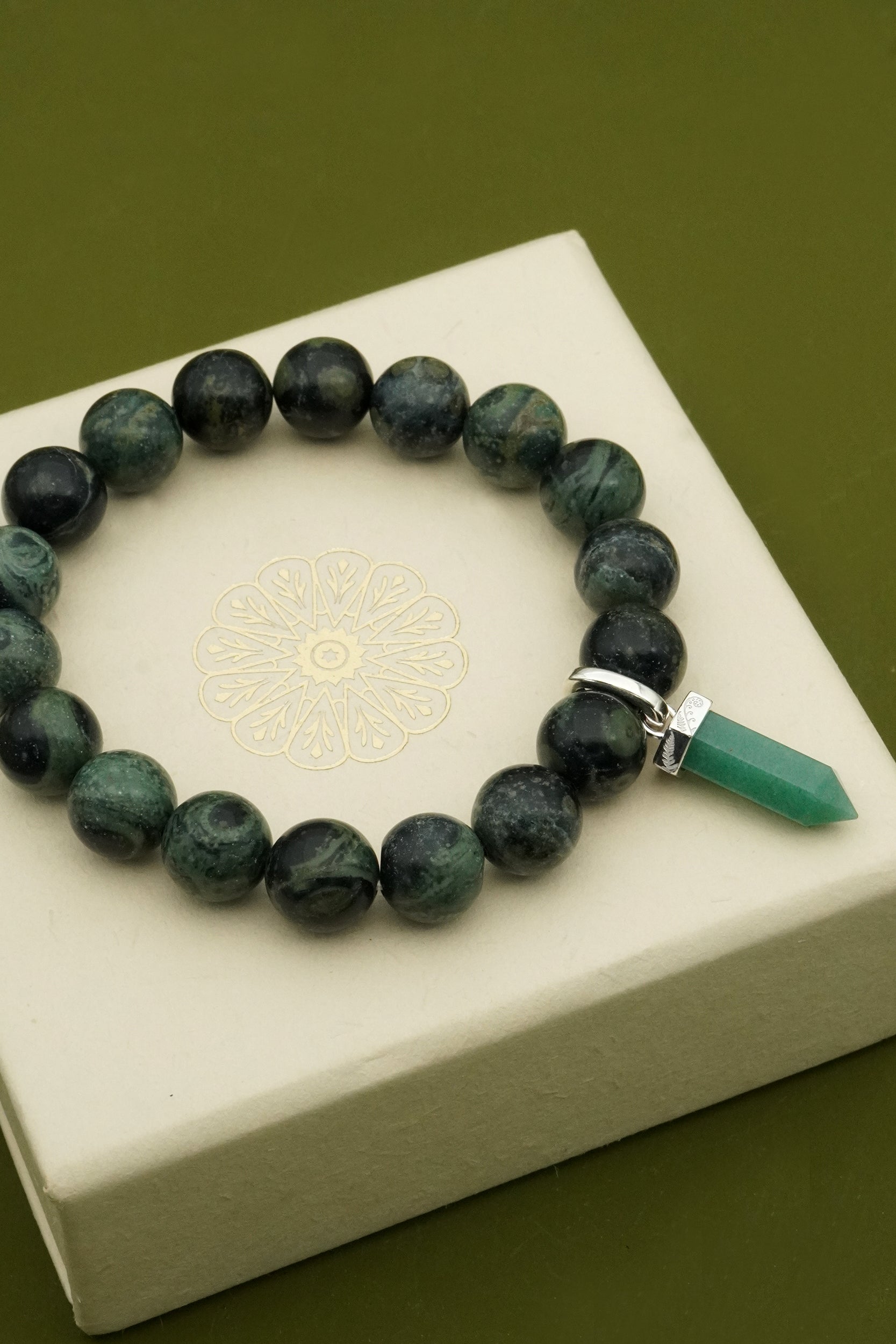 Green crystal beaded bracelet with a Silver Fern charm on a white box against a green background