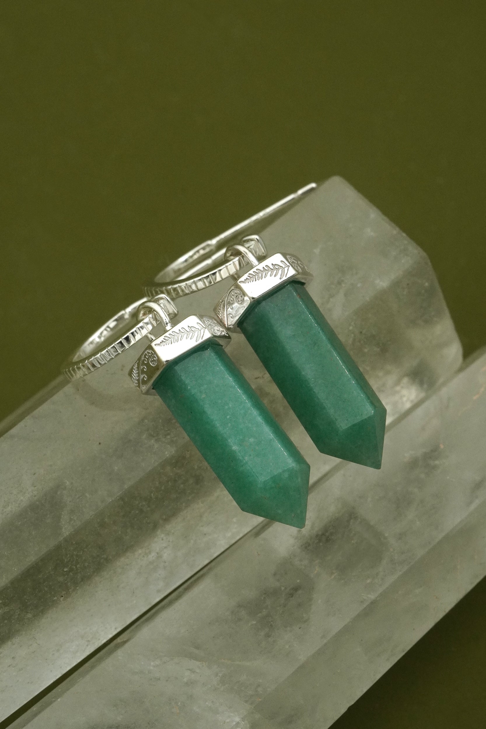Silver earrings  with green gemstones on a crystal surface