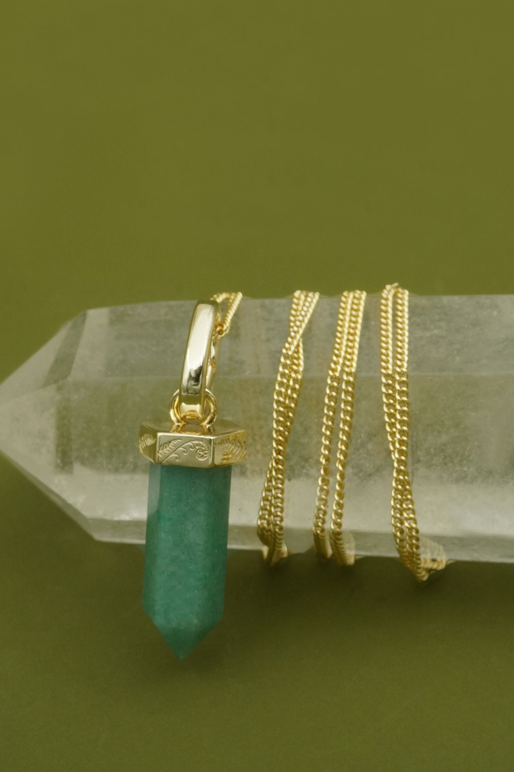 Gold necklaces with a green pendant  and NZ fern detailing  on a crystal base against a green background