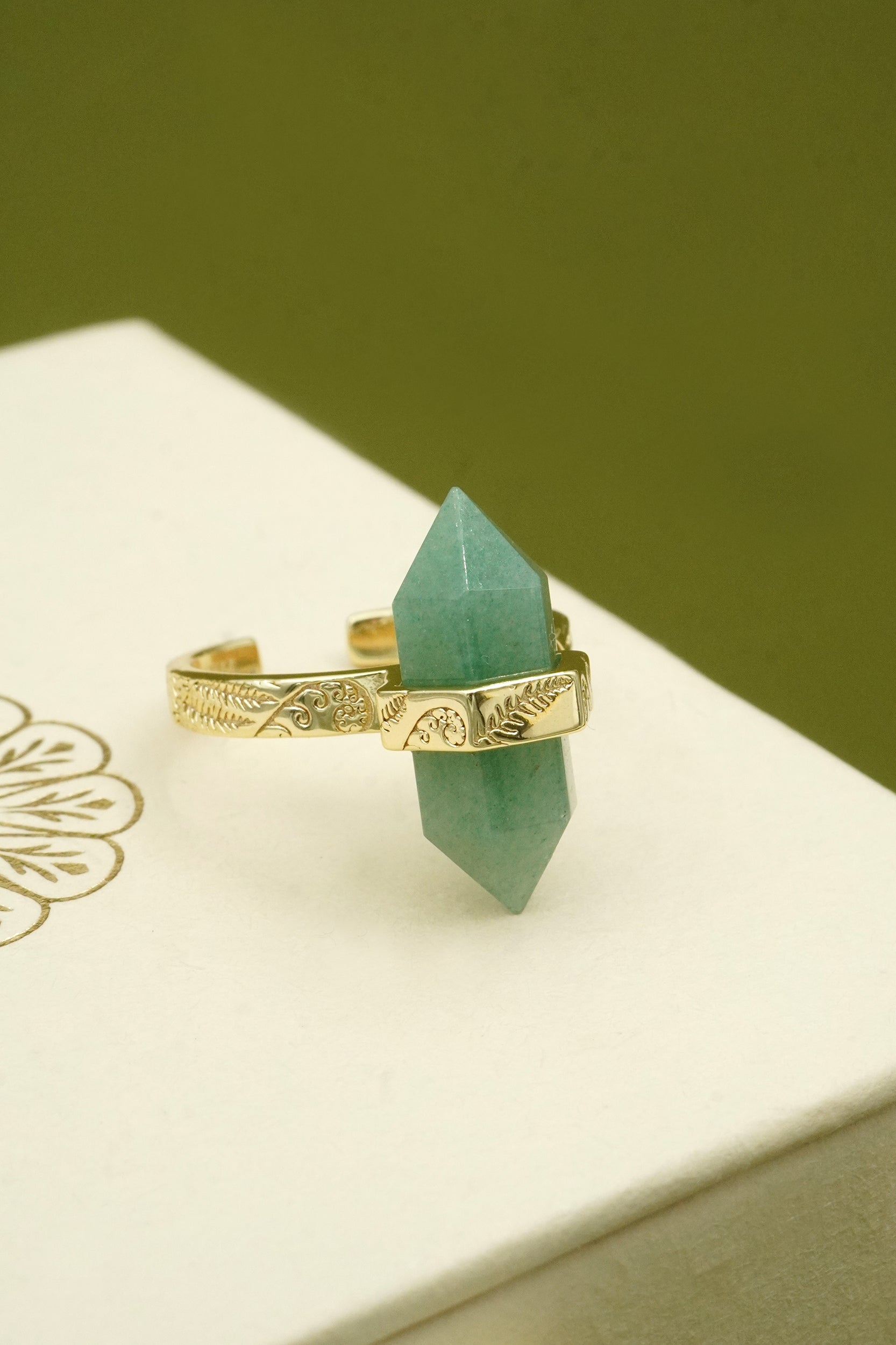 Gold ring with a green crystal on a white surface with a green background