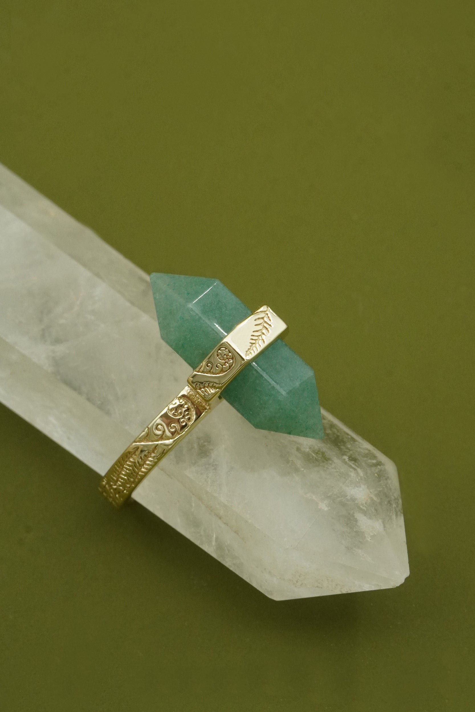 Gold ring with green gemstone and native NZ koru and fern detailing on a crystal against a green background